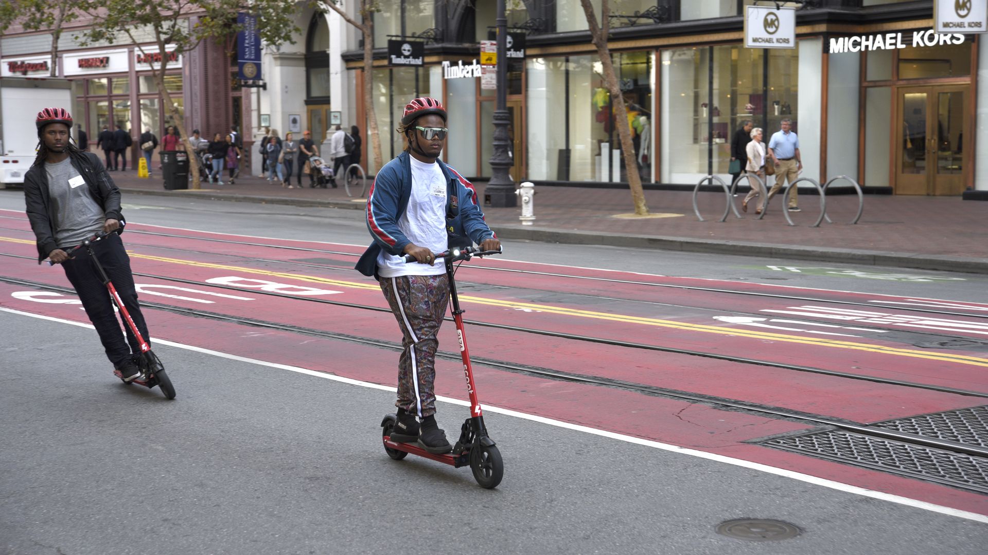 Photo of two people riding red Scoot scooters on Market Street in San Francisco. 