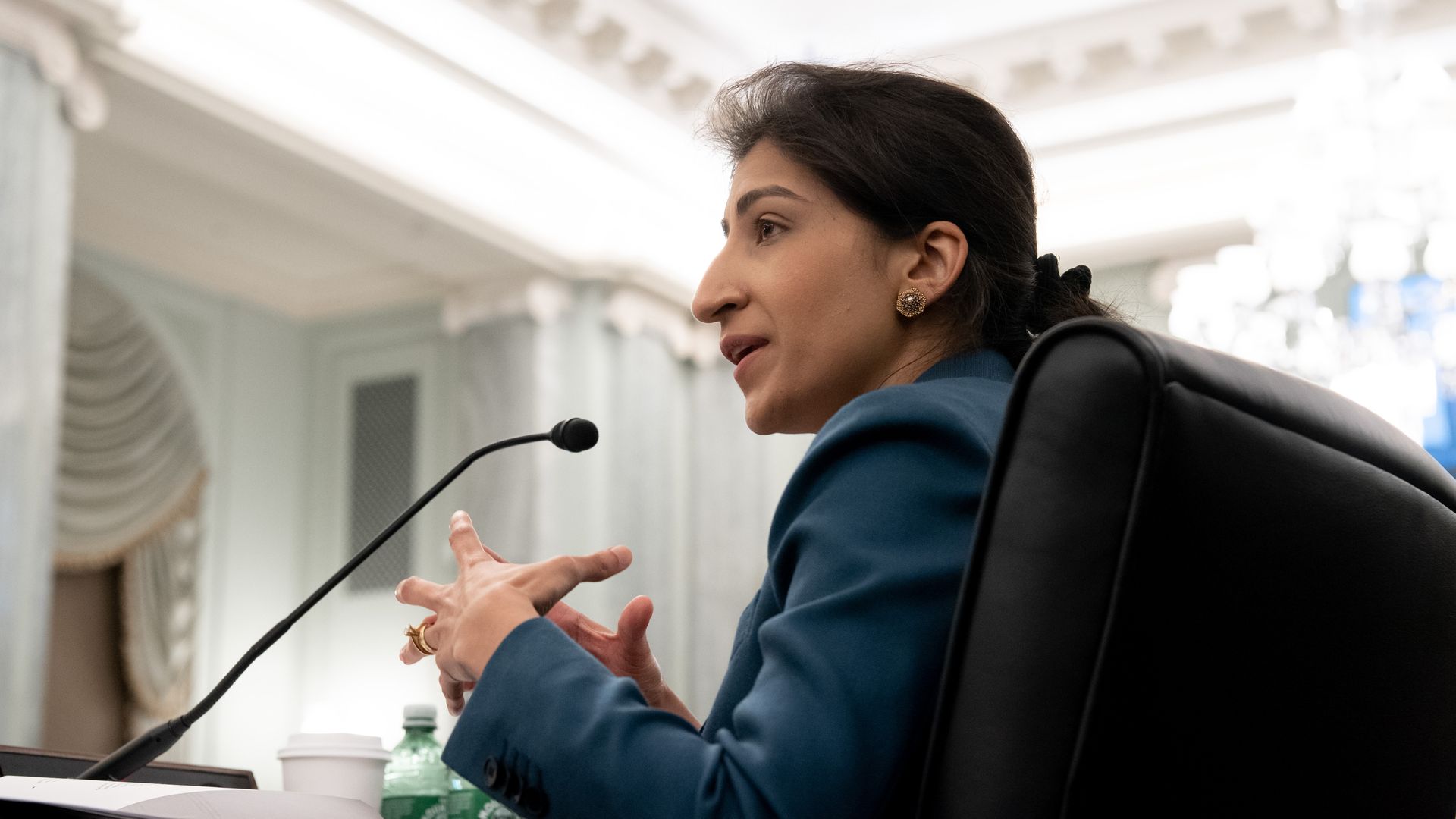 FTC Chair Lina Khan sits in a chair in front of Congress.