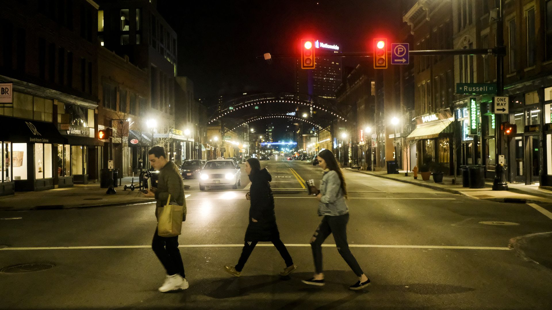 Three people cross High Street in a crosswalk in the Short North at night