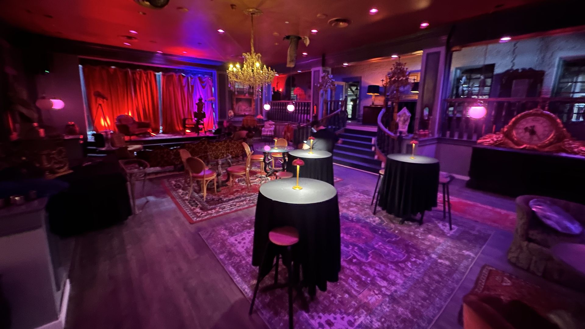 A darkly lit Parisian-style speakasy with vintage satin chairs, chandelier and red, purple and deep blue tones.