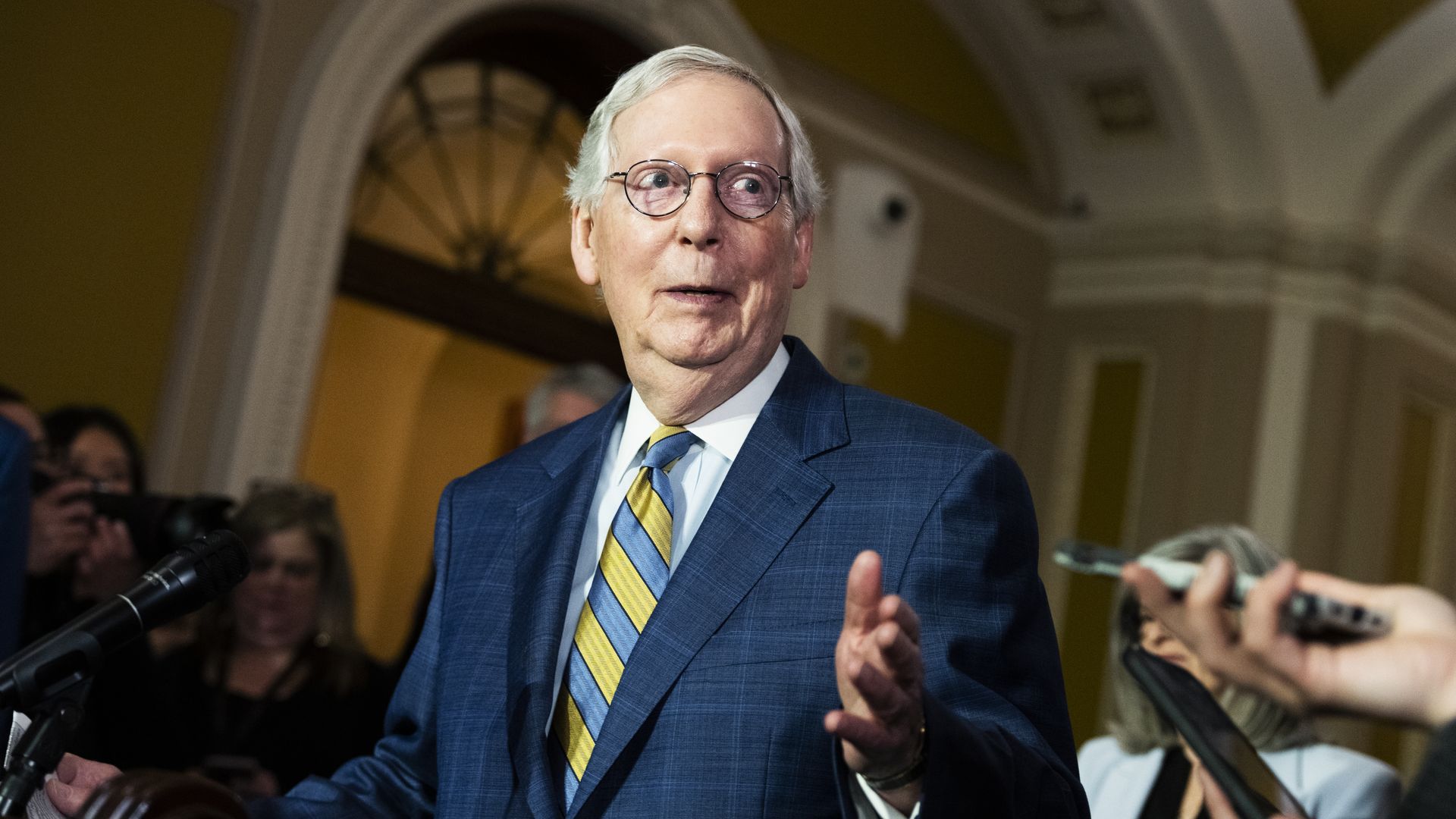 Senate Majority Leader Mitch McConnell, wearing a light blue suit, white shirt, blue-and-yellow striped tie and glasses, speaks to reporters at the Capitol.