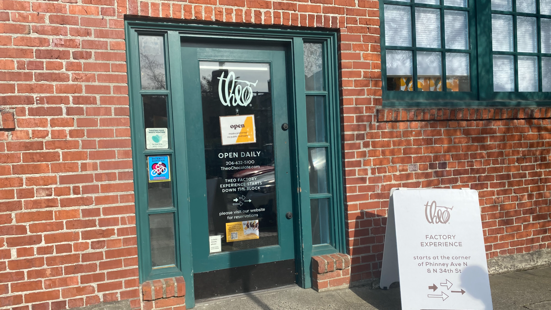 The green front door of Theo Chocolate's Fremont flagship store, surrounded by red brick.
