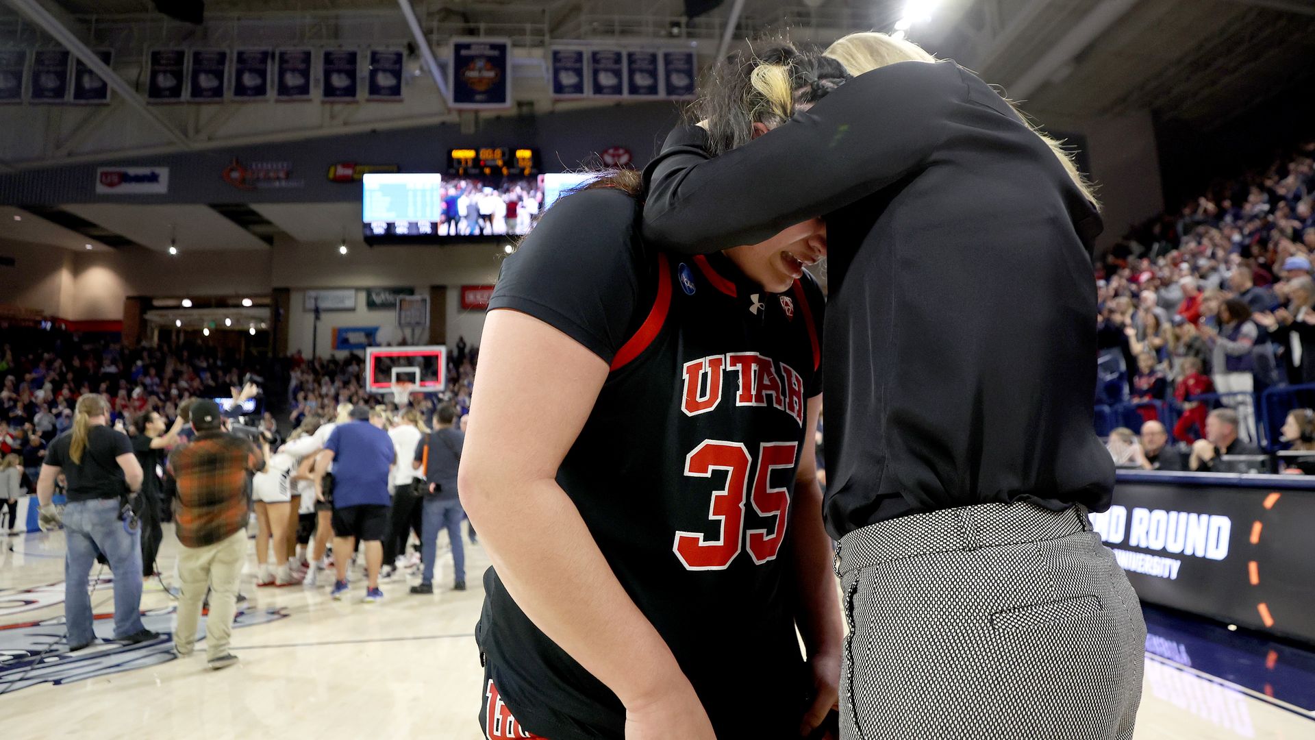 A coach hugs a University of Utah basketball player on a basketball court. 