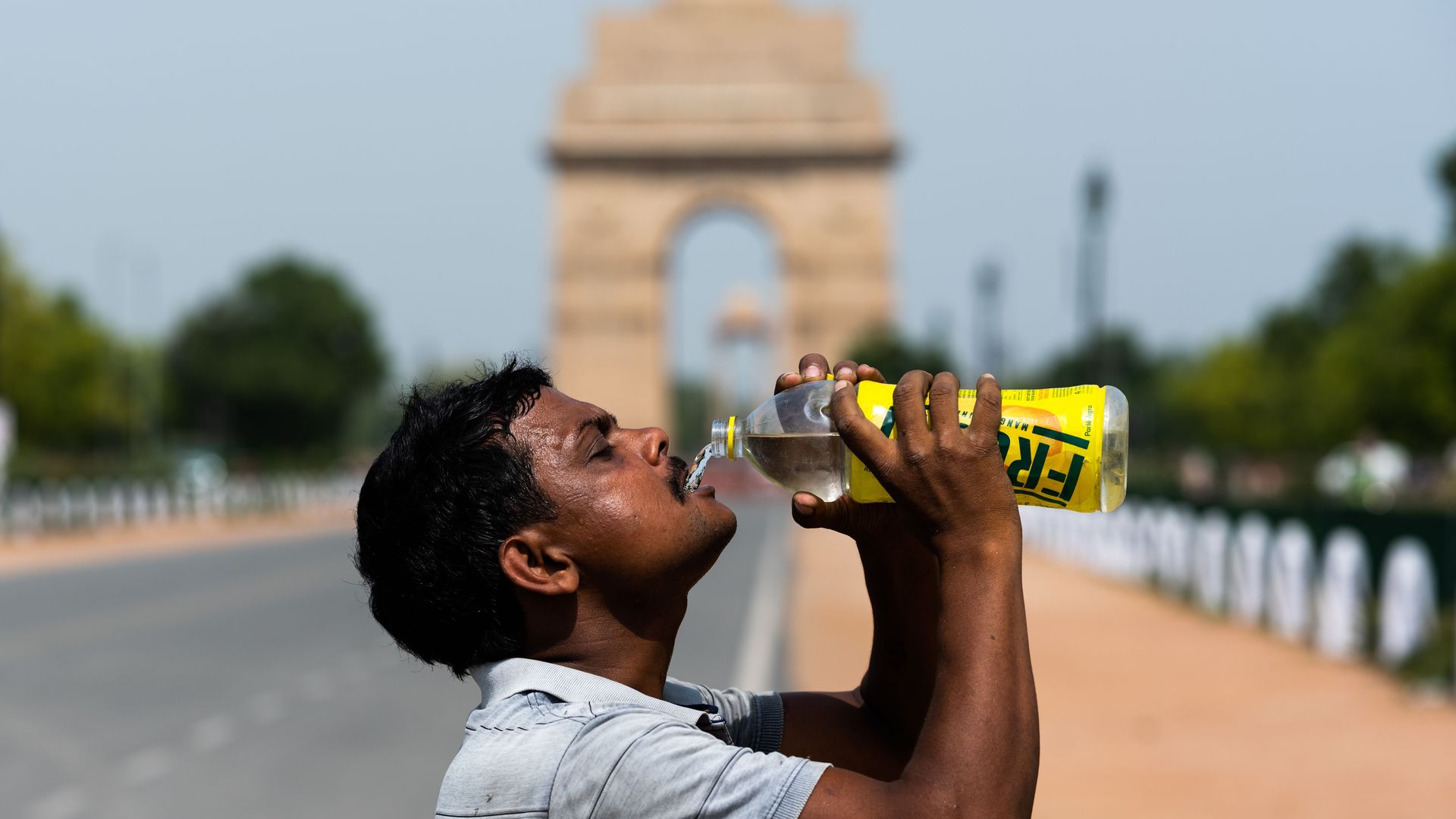 Man drinking water in front of a statue on a hot day.