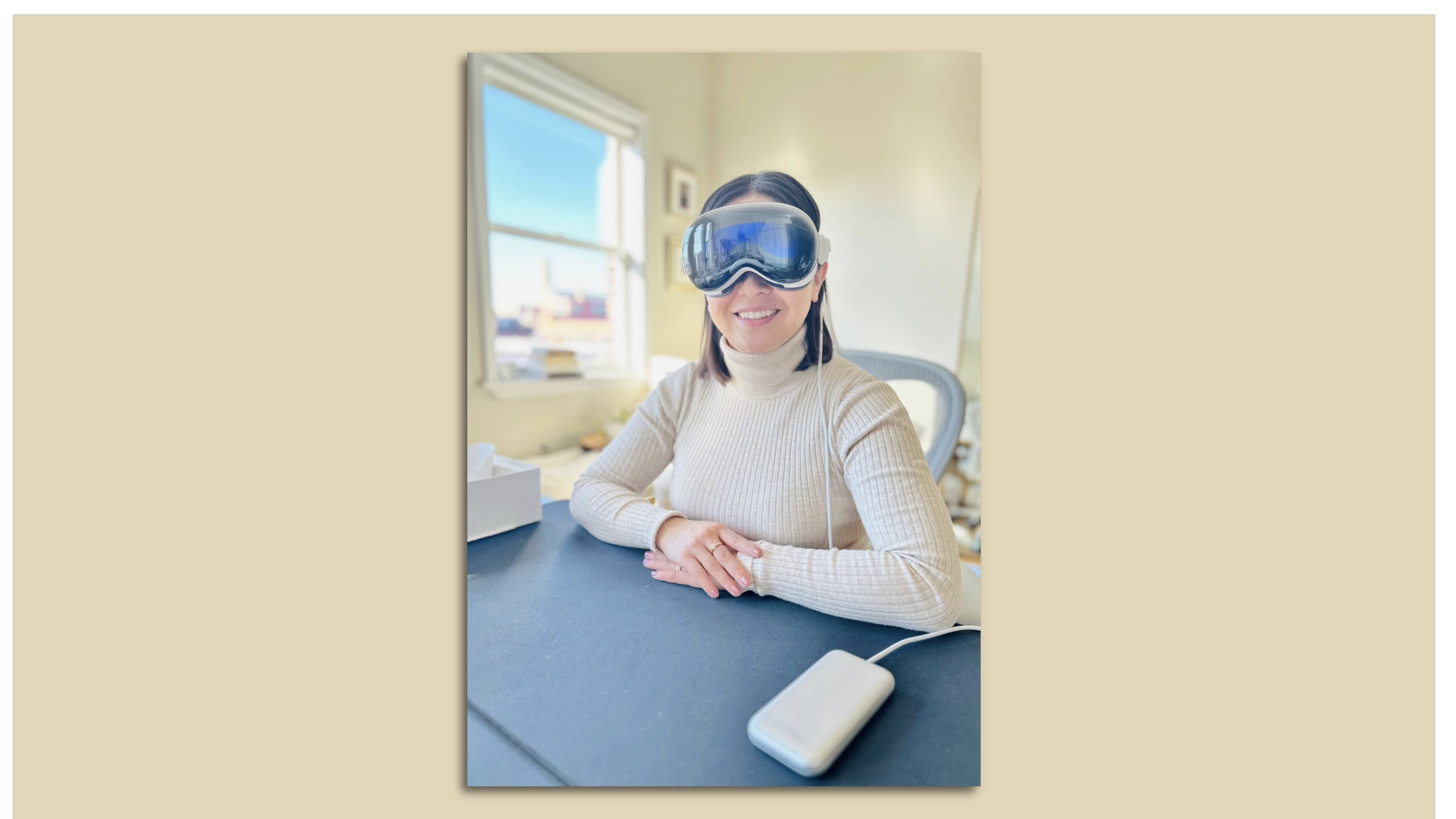 Photo of a woman sitting at a table wearing a pair of Mixed Reality goggles from Apple