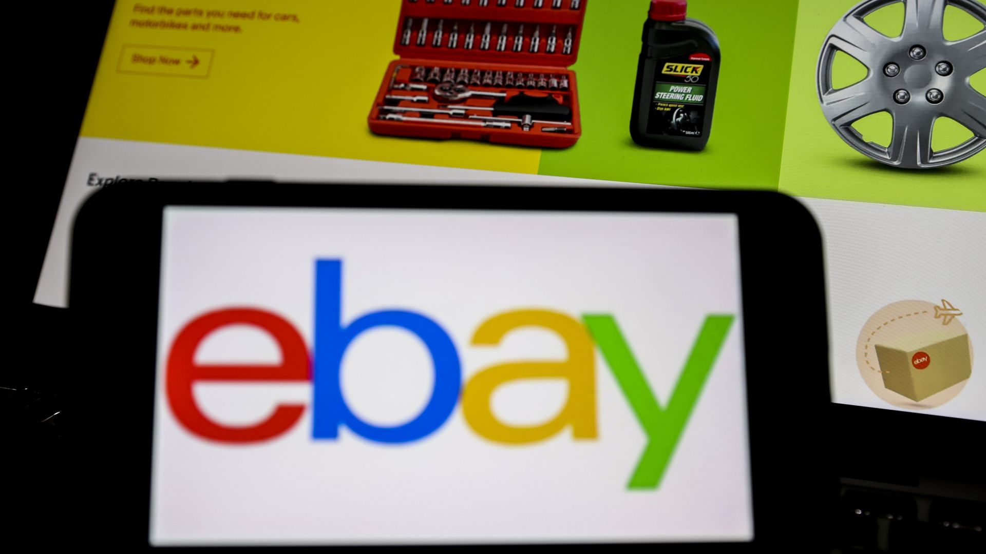 A photo illustration of the eBay logo on a phone, with a computer showing the eBay home page in the background.