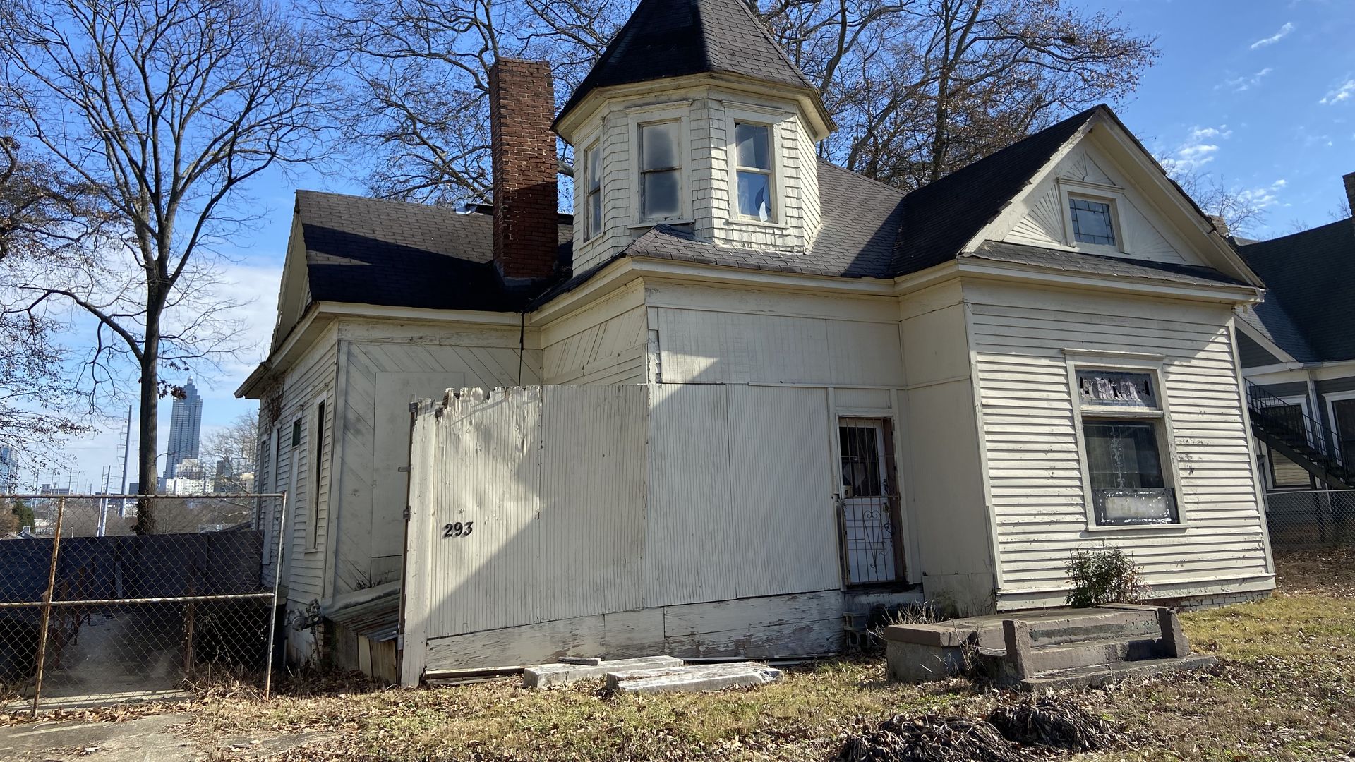 A photo of an old vacant white house with a prominent turret like feature on the second floor