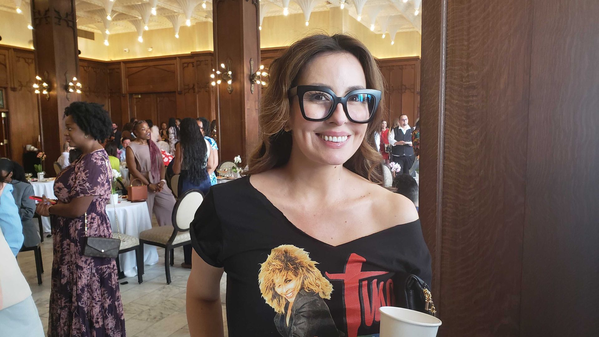 Food personality host Monti Carlo smiles wearing thick black glasses and a Tina Turner T-shirt.