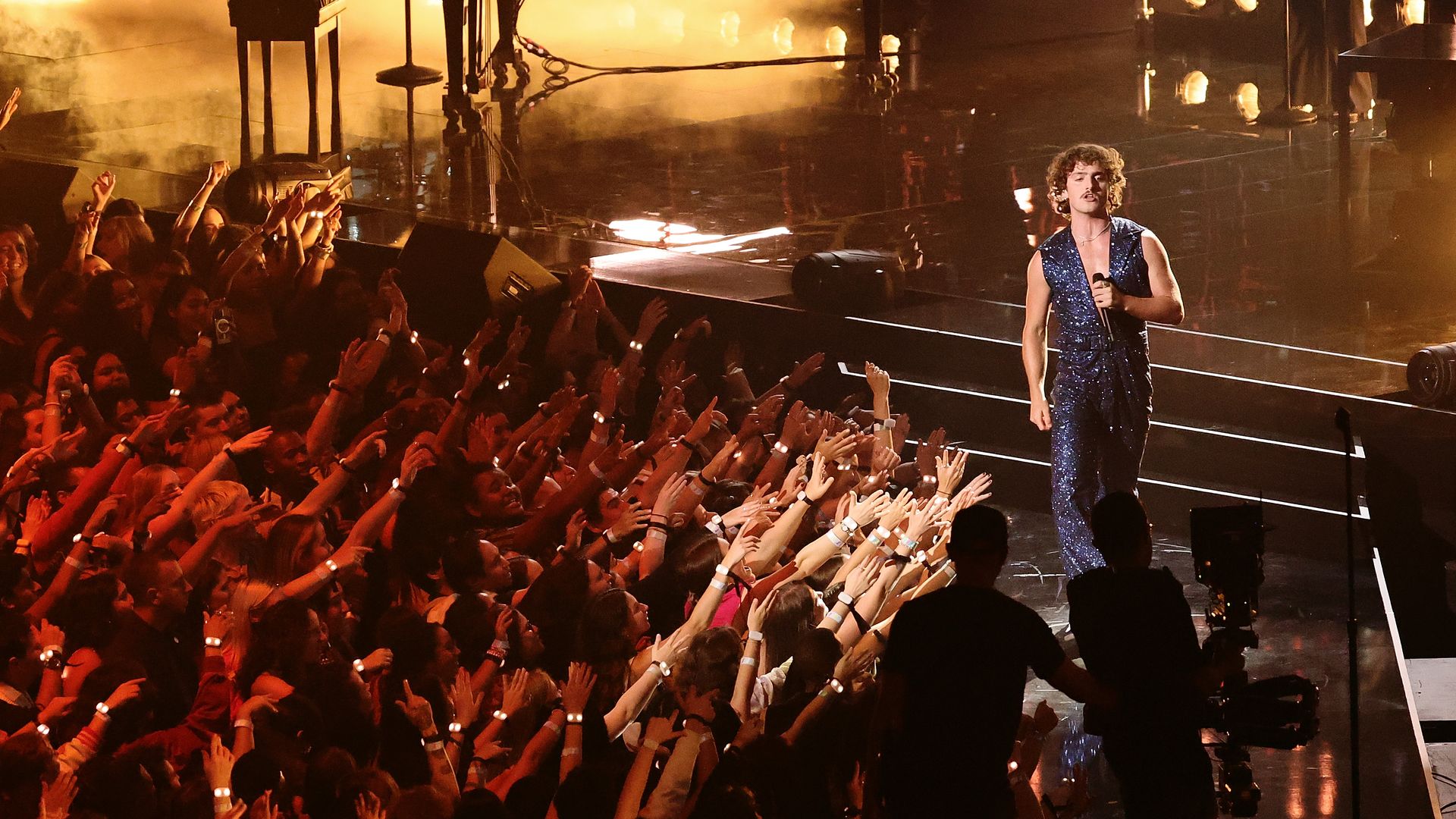 Benson Boone walks performs on stage surrounded by fans. 