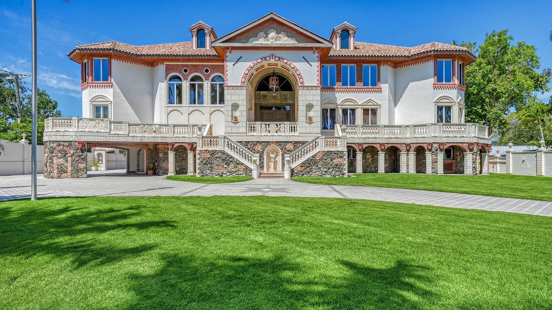 A mansion with an orange tile roof, arched windows and a wraparound terrace.