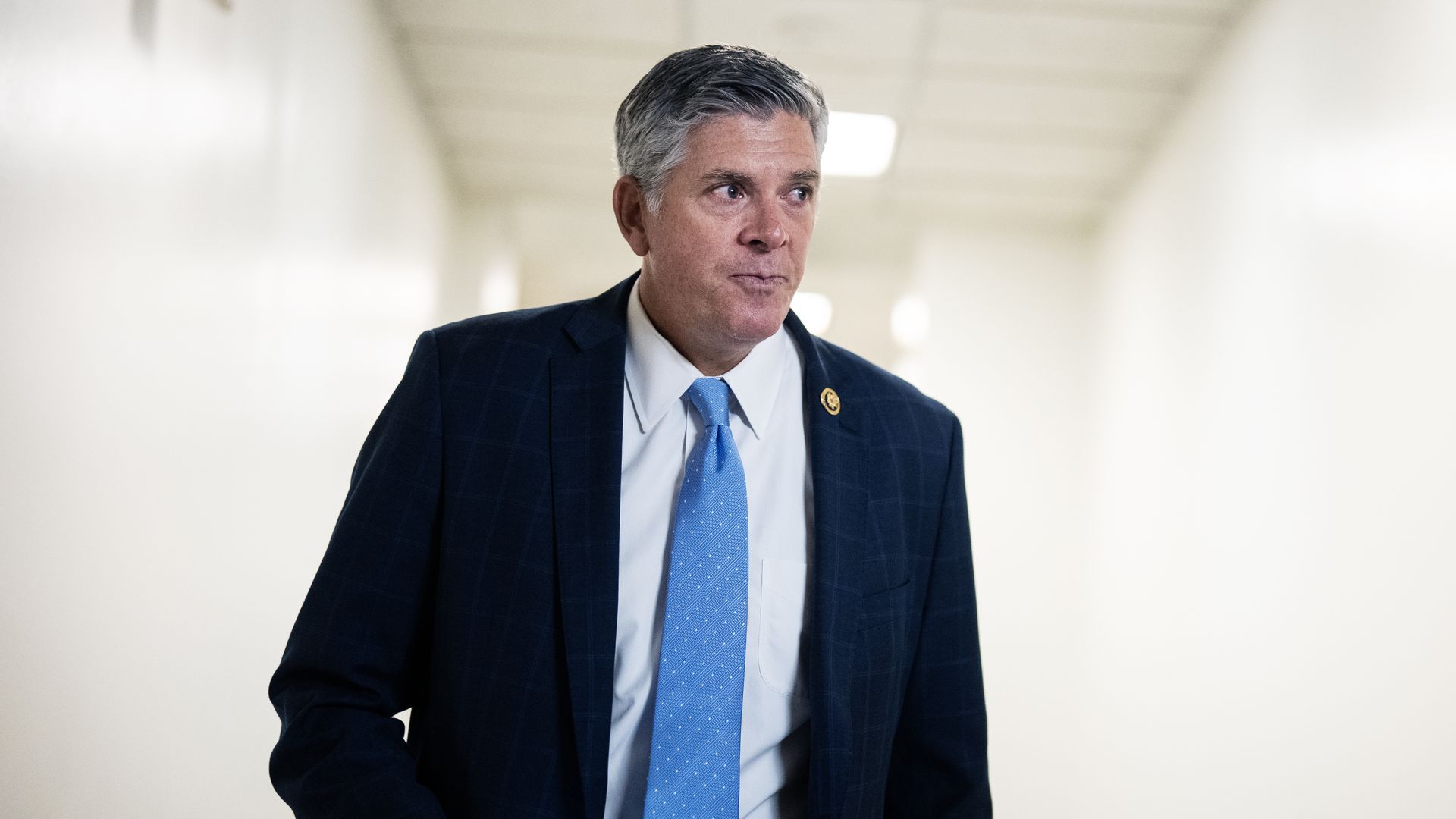 A person in a blue suit and tie walks down a brightly lit corridor