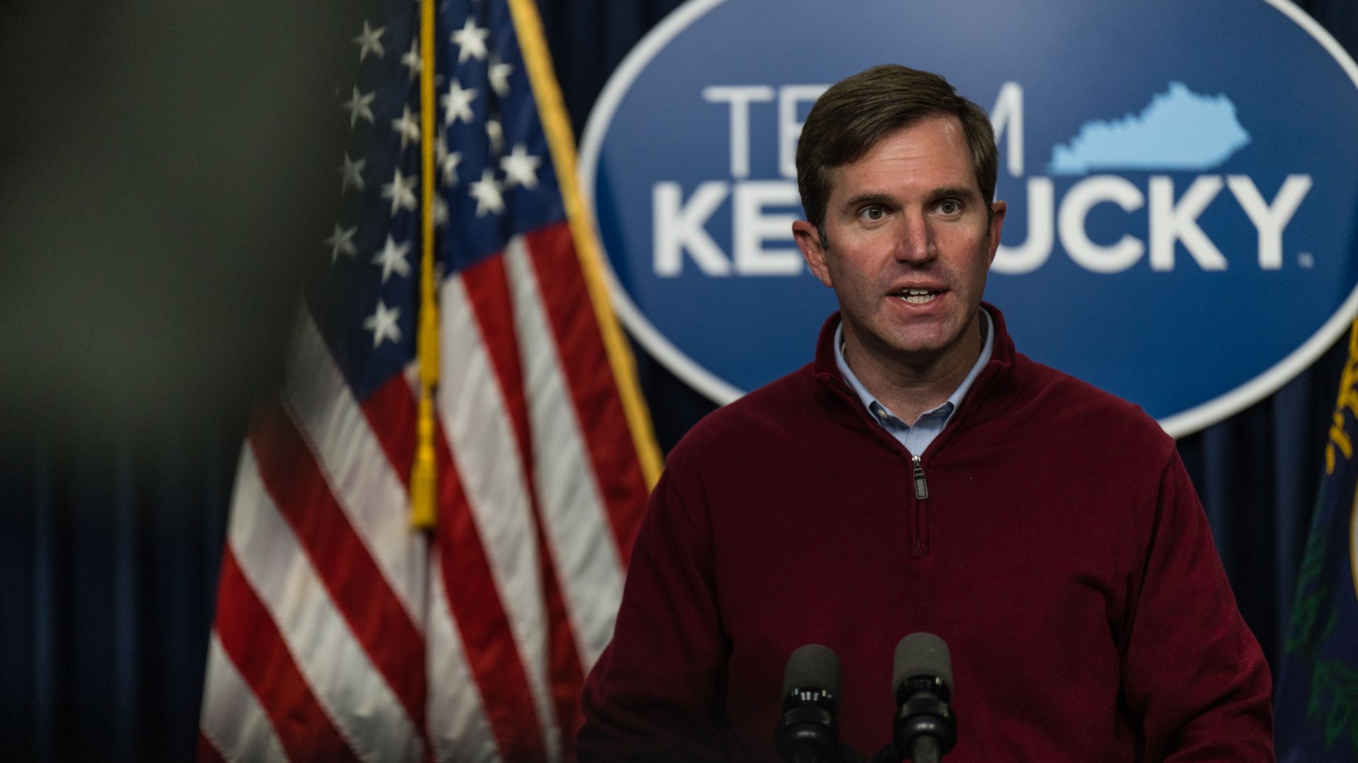 Photo of Andy Beshear speaking from a podium in front of a Team Kentucky sign