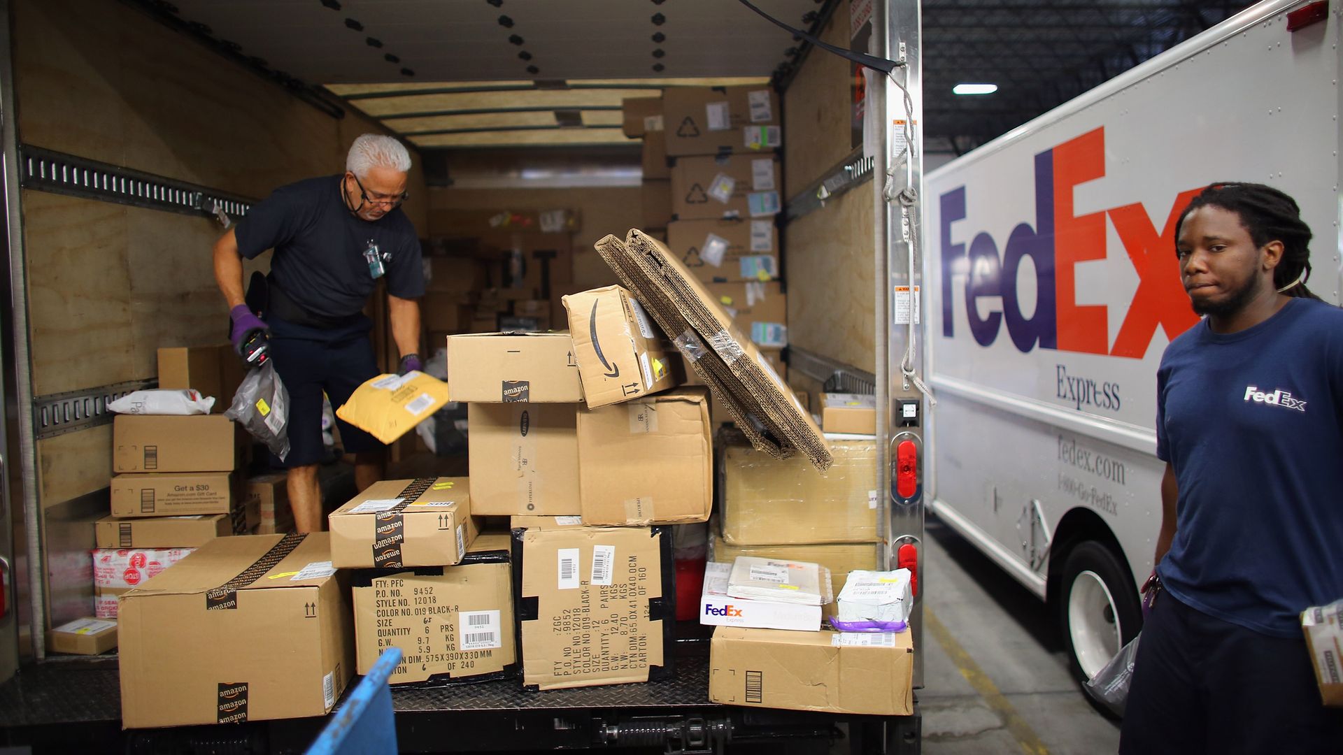 Two men load packages onto a large truck