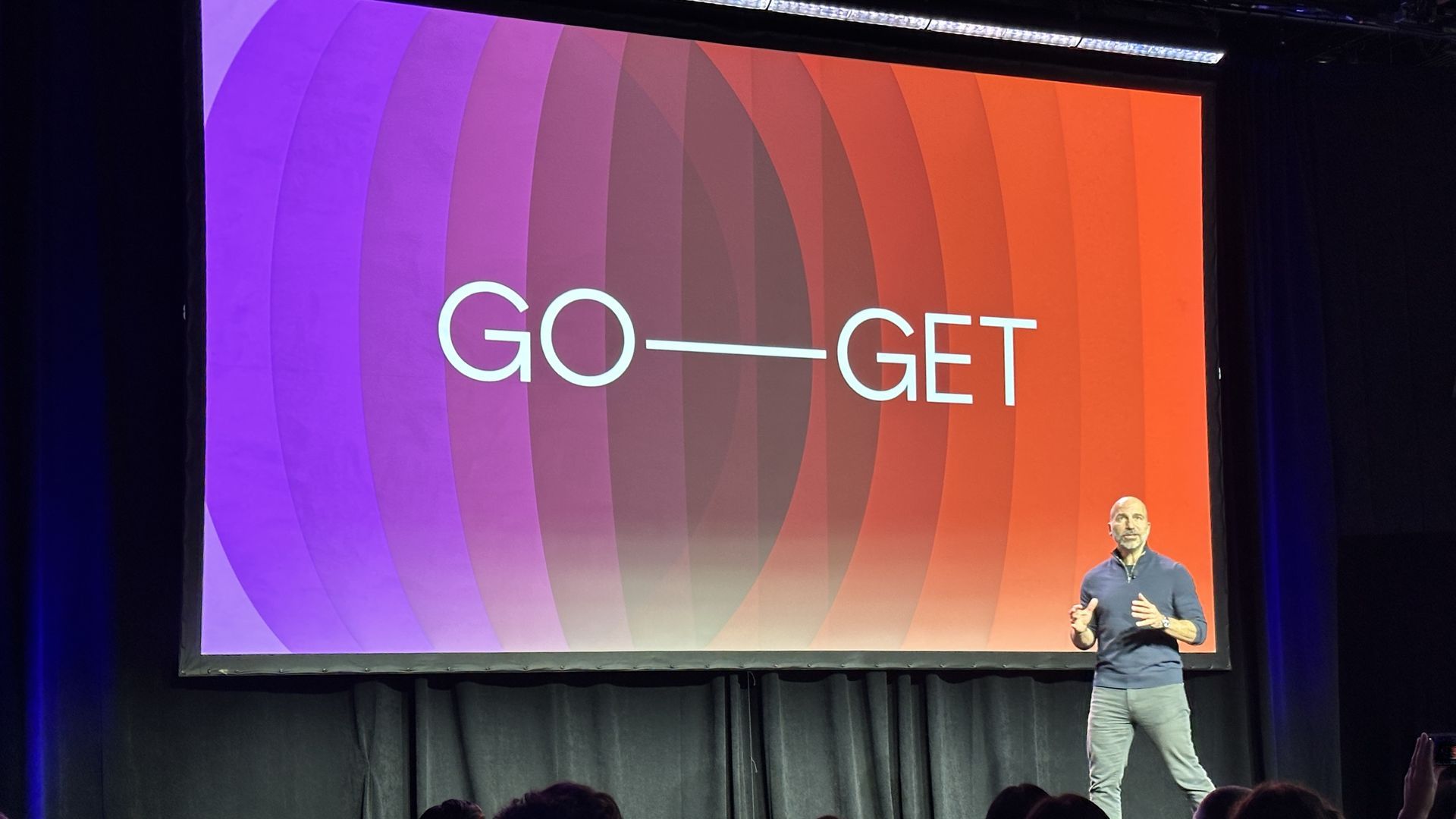 photo of a male executive walking across a stage with a colorful screen behind him with the words "Go," and "Get"