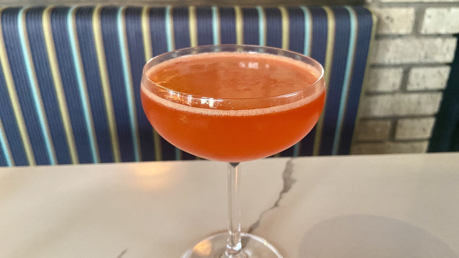 A peachy colored cocktail in a coupe glass