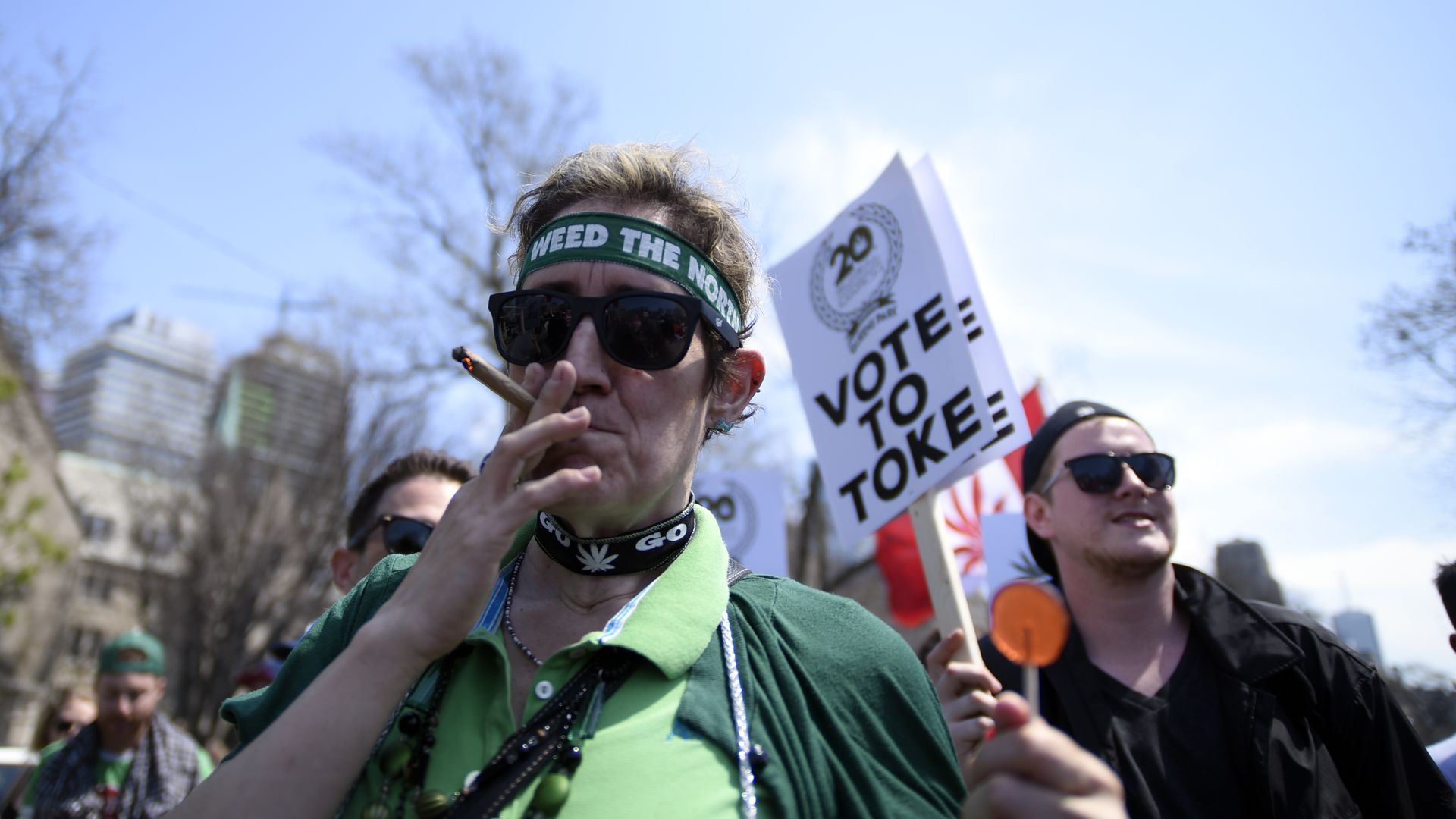 A man smoking weed in Canada, with a sign behind him that says, "Vote to Toke."