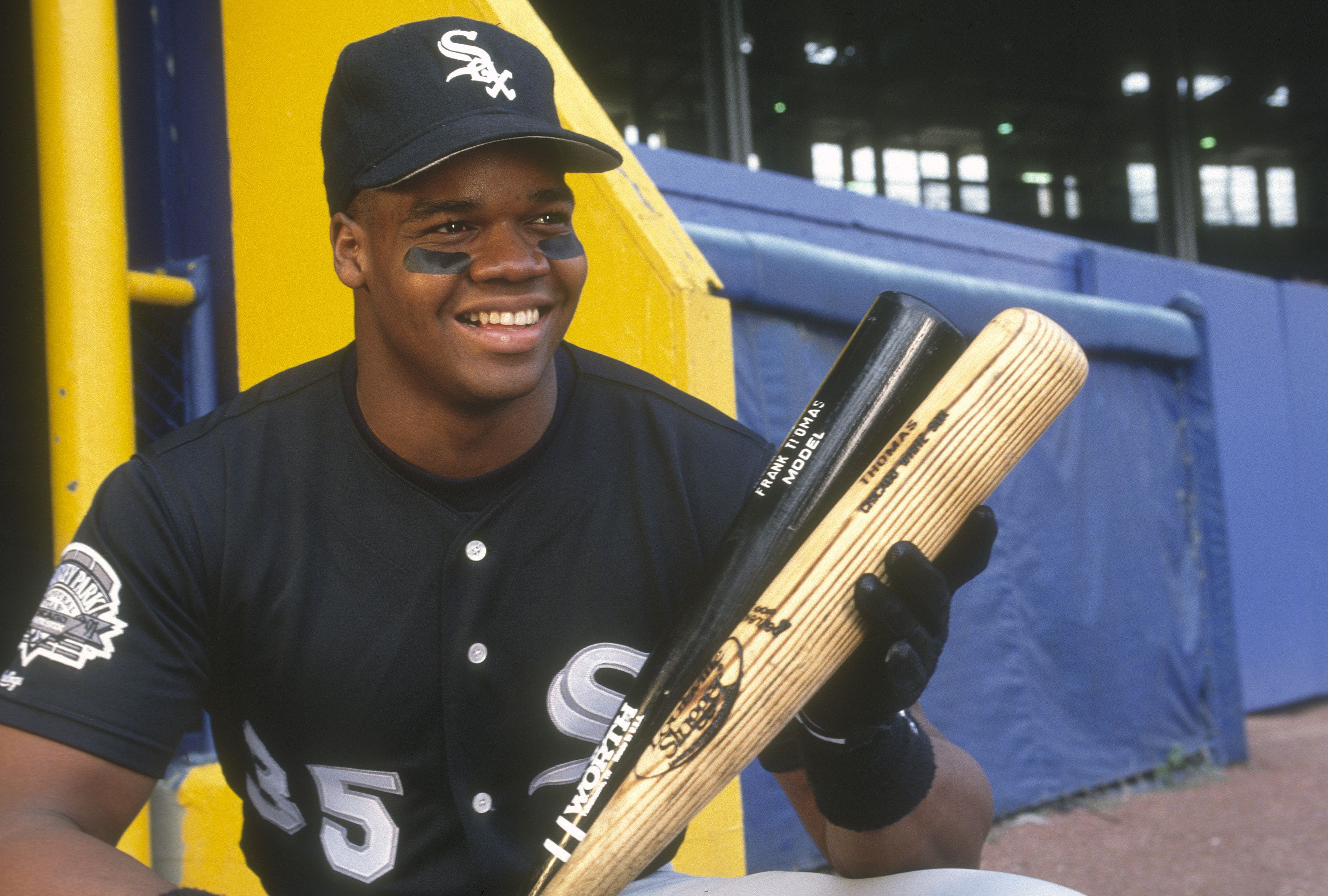 Photo of a baseball player in uniform holding two bats. 