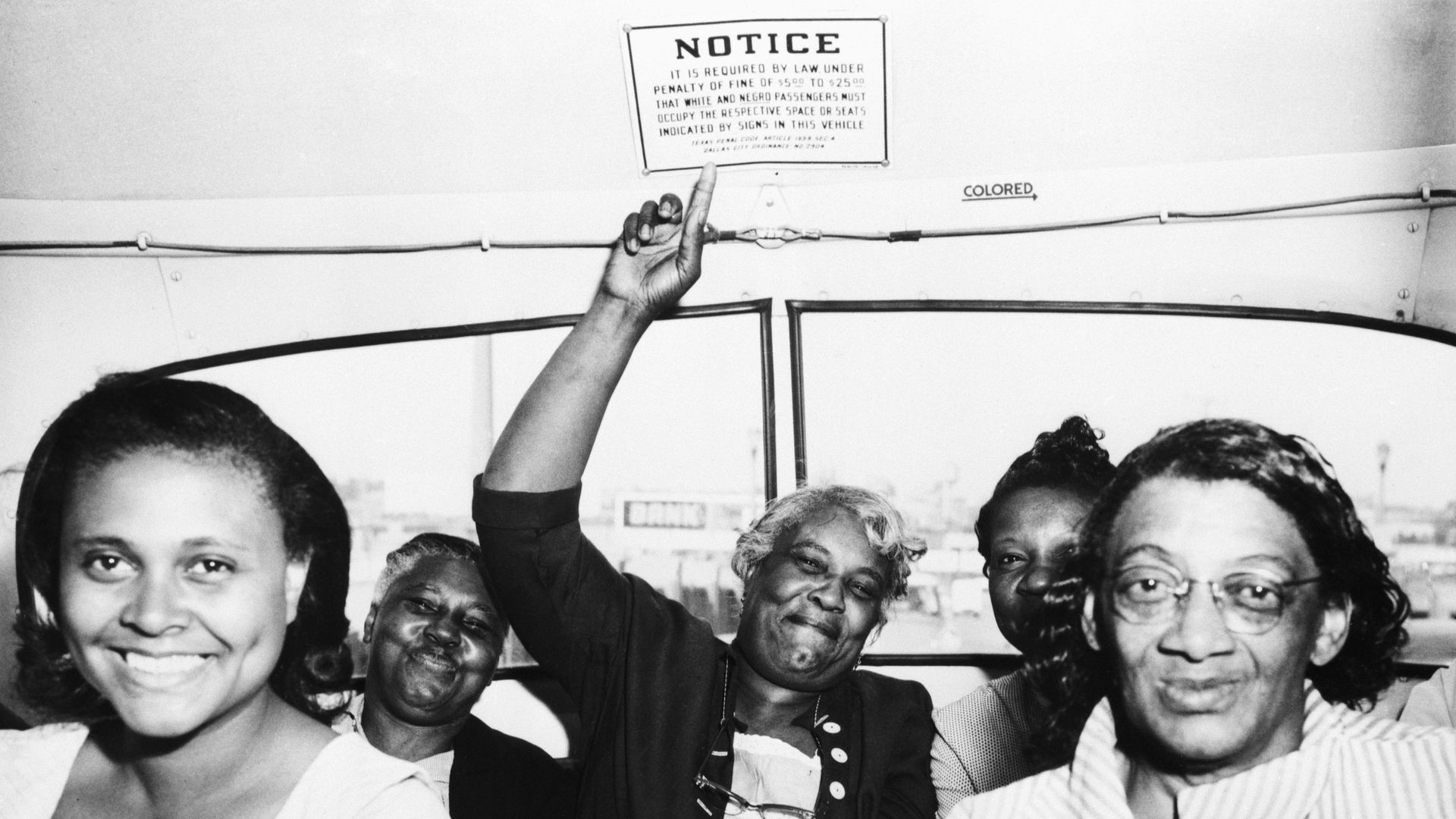 A photo of five Black women pointing to a segregation sign. 
