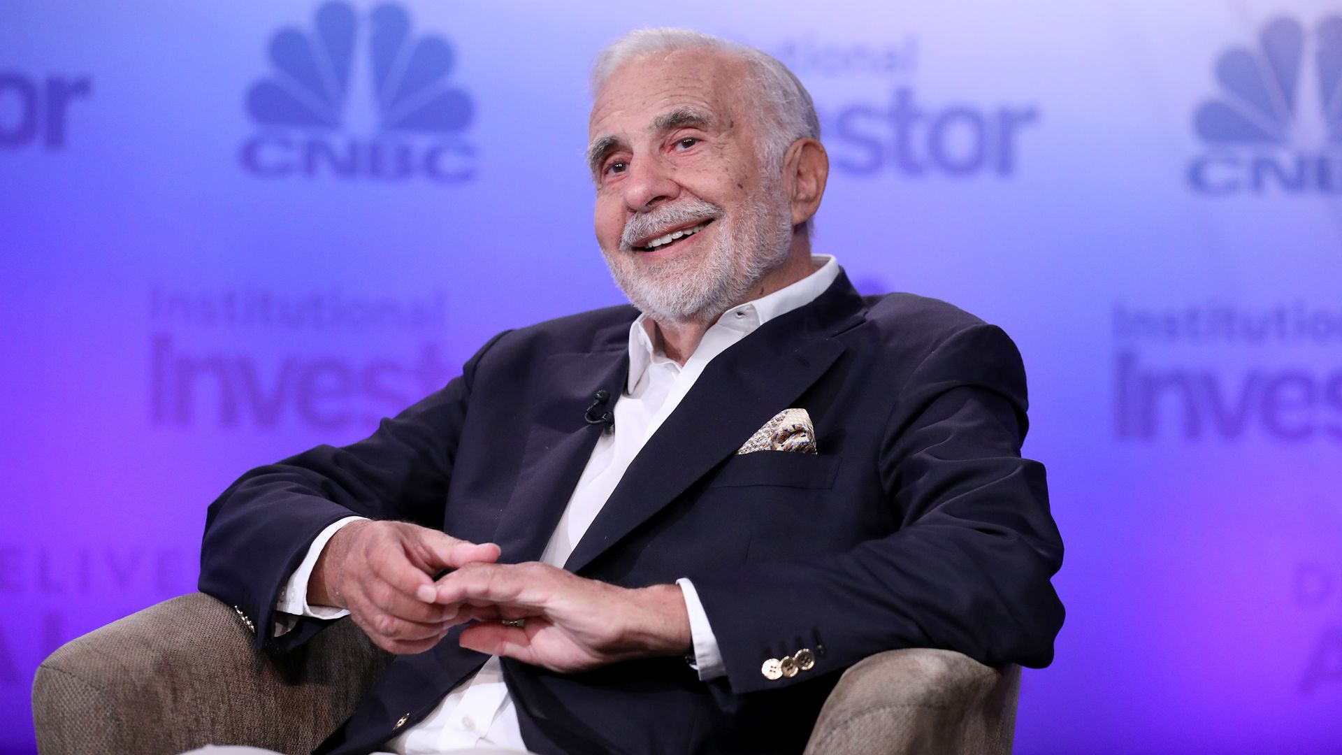 Carl Icahn sitting in a chair smiling on stage at an event