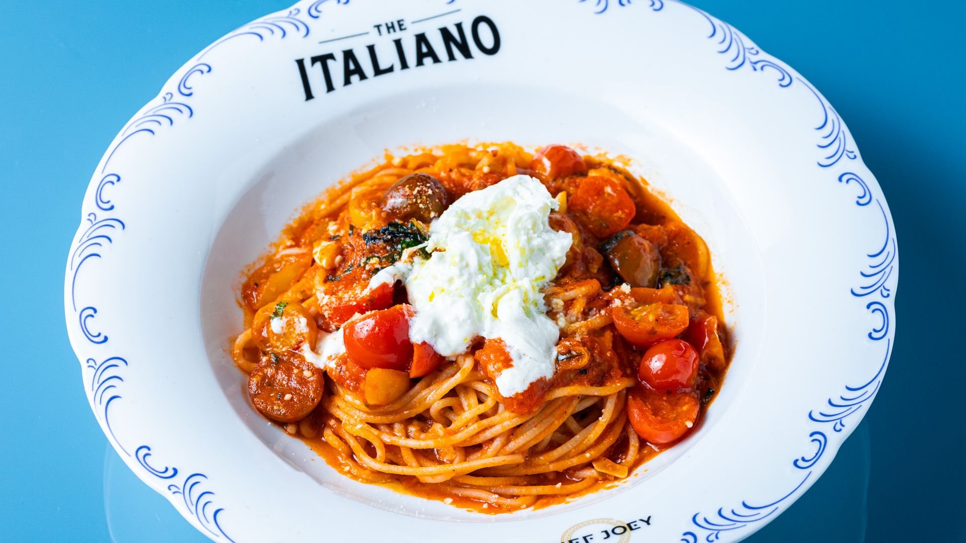 Plate of spaghetti with tomato sauce, cherry tomatoes, sausage slices, and a dollop of white cheese on top. Plate is white with blue decorative patterns and text "THE ITALIANO" and "CHEF JOEY".