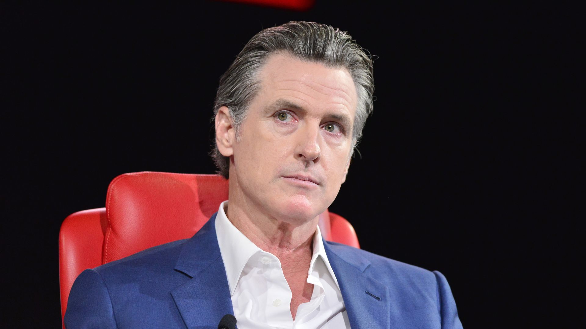 Photo of Gavin Newsom looking to his right as he sits in a red chair
