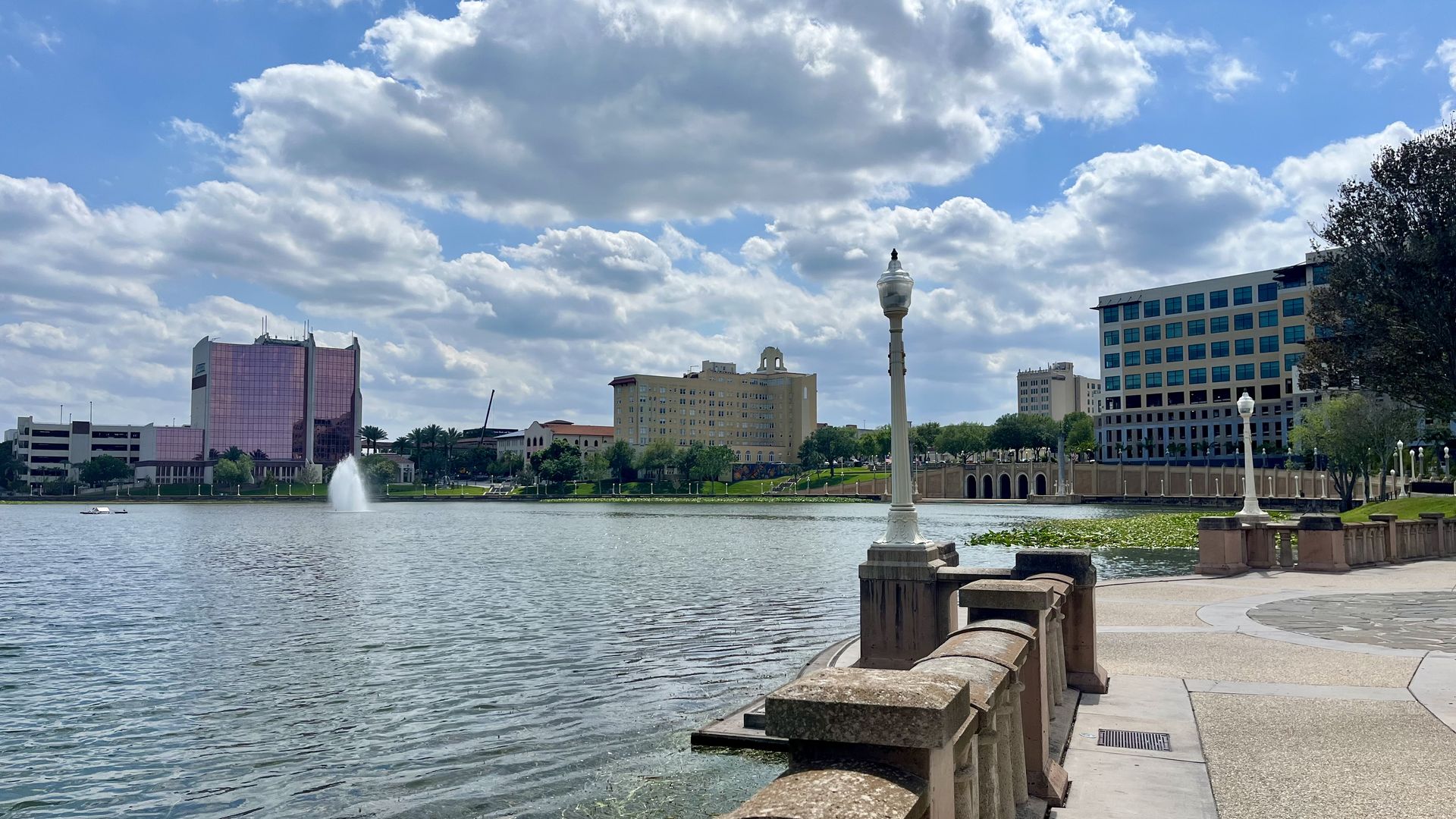 A view of a lake and several buildings from a paved walking path along the lake's perimeter. 