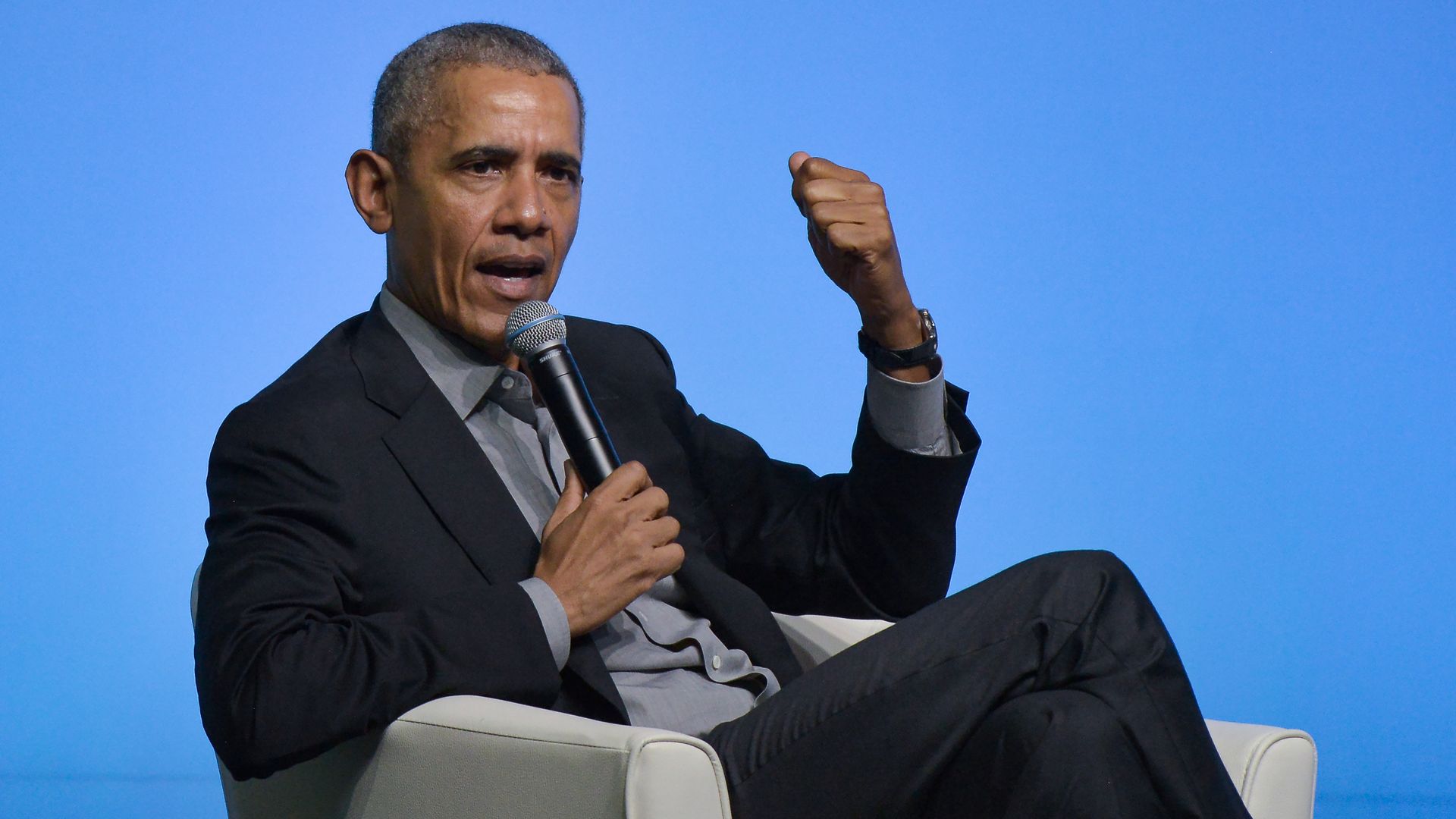 In this image, Obama sits while gesturing 