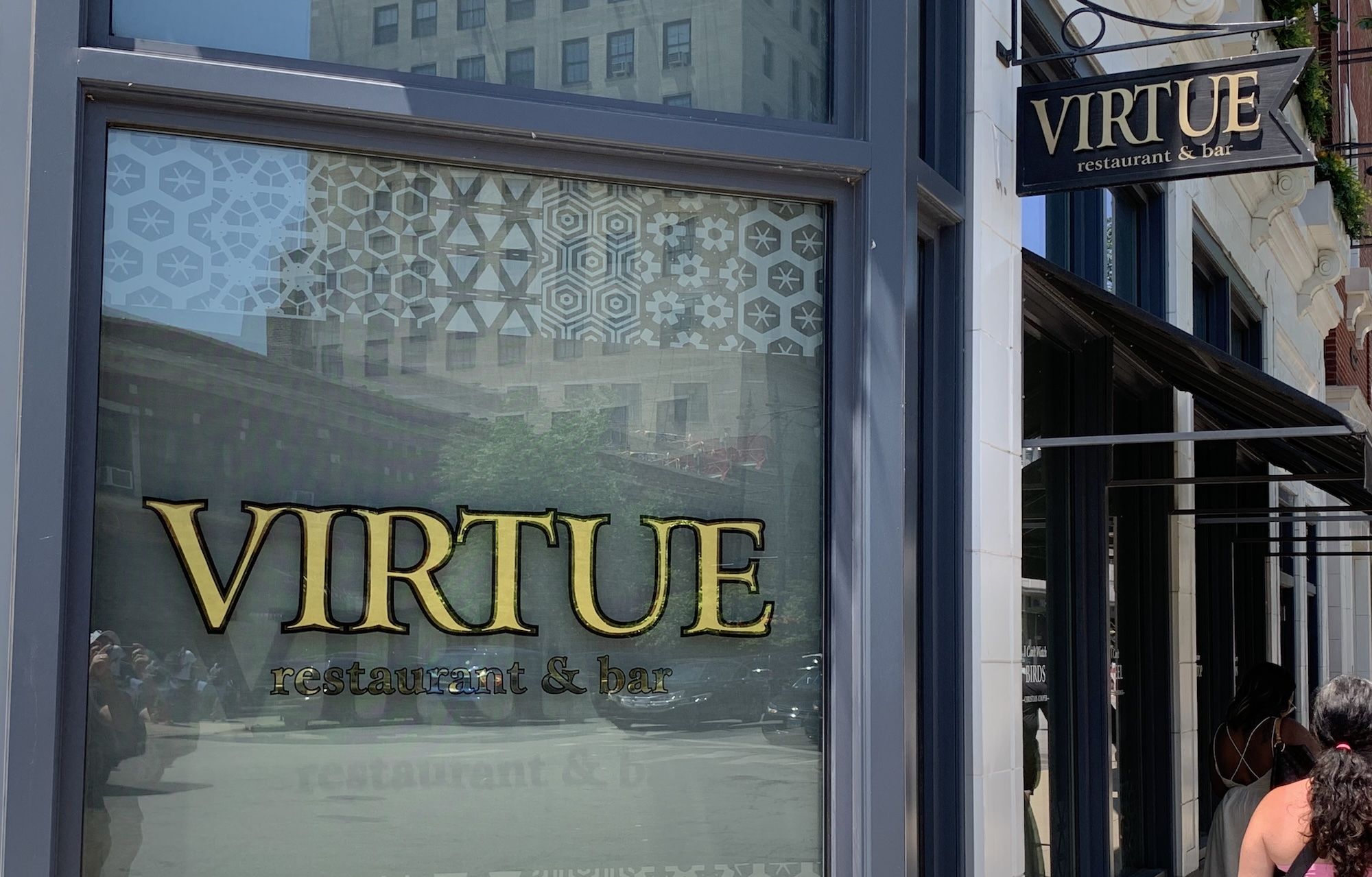 Exterior of a blue-framed restaurant storefront for "Virtue" with a large gold "VIRTUE" sign on a frosted patterned window and a hanging sign reading "VIRTUE restaurant & bar".