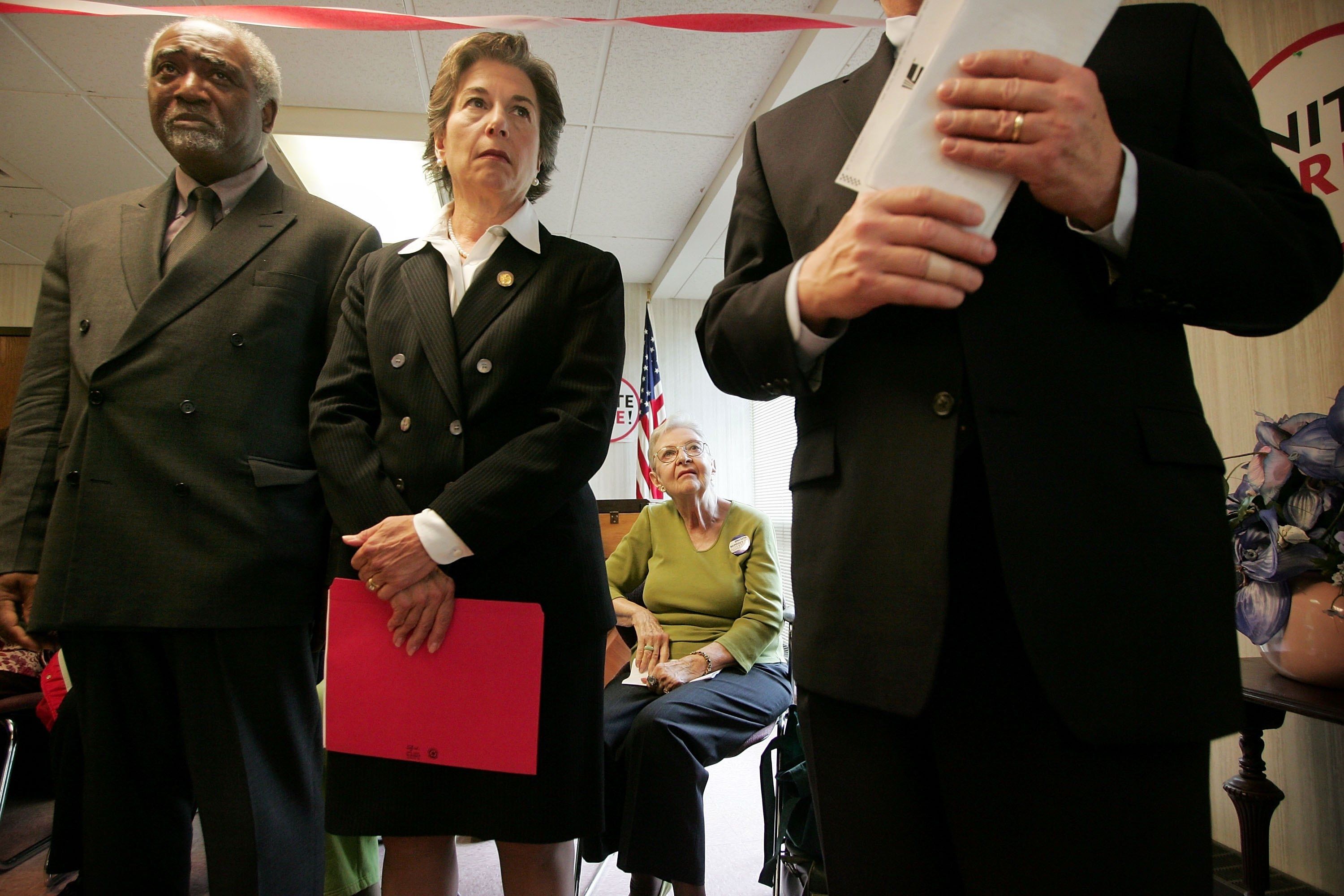 US Reps. Danny Davis and Jan Schakowsky who's holding a red file folder next to a man in a suit whose head is not in frame.