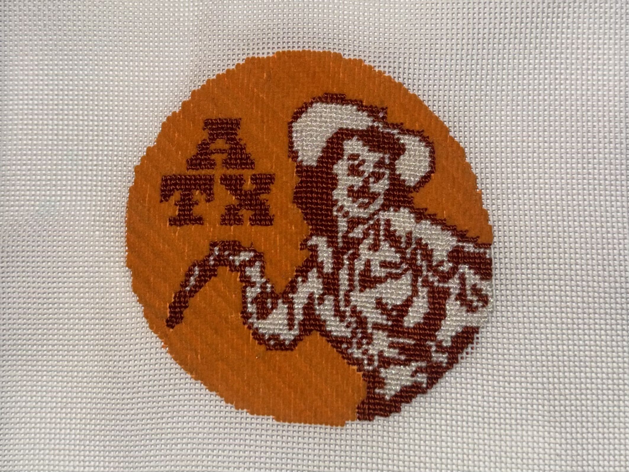 Orange circular embroidered patch on white fabric, depicting a maroon-and-white Santa Claus figure with hat and bag on the right, and the letters THE to the left.