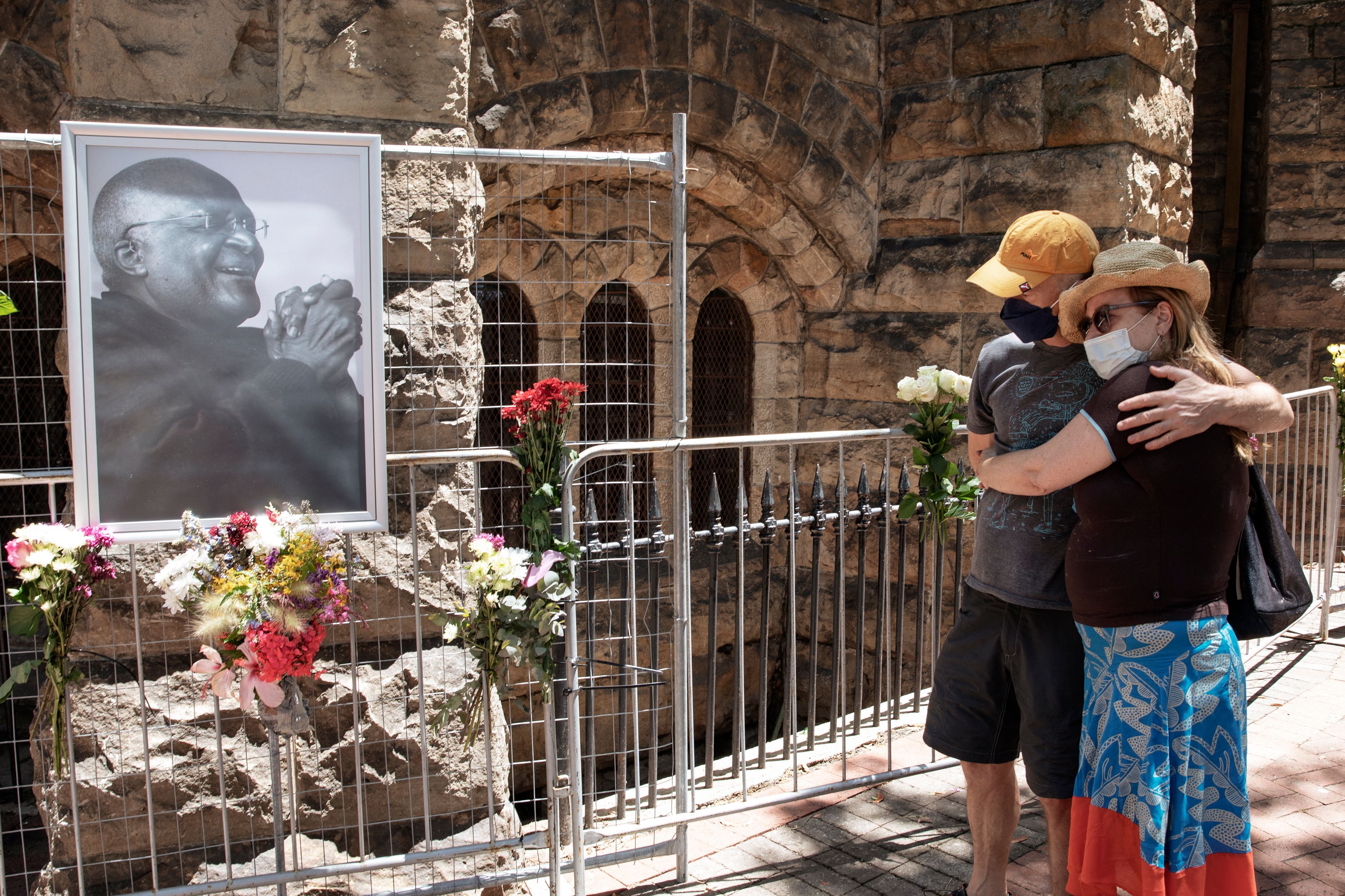 A couple stands by a picture of the late South African Nobel Peace Price Archbishop Desmond Tutu on the wake of his death outside St. George's Cathedral in Cape Town on December 26, 2021.