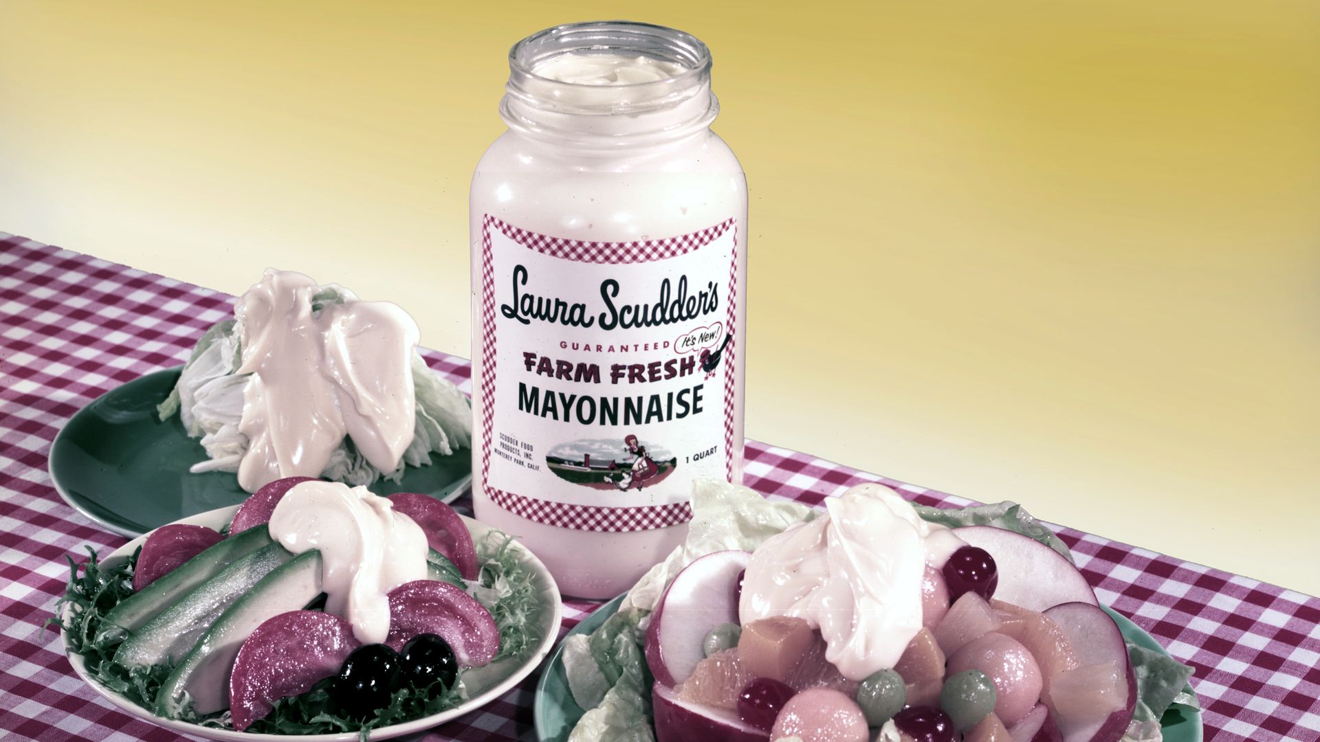 An open jar of mayonnaise next to plates of veggies on a gingham tablecloth