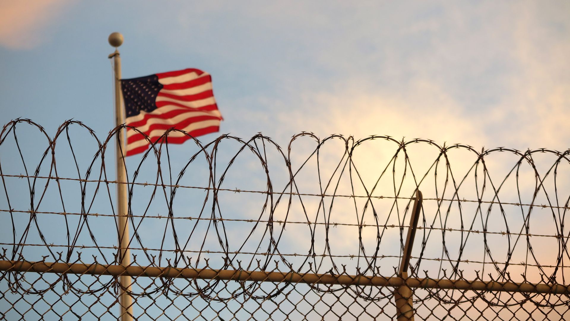 Photo of an American flag flying on a pole behind barbed wire