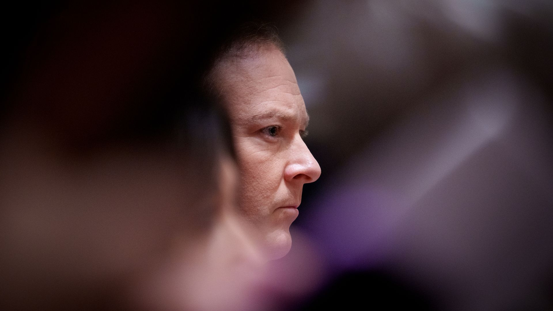 A person's face is framed in the background by blurred people in the foreground