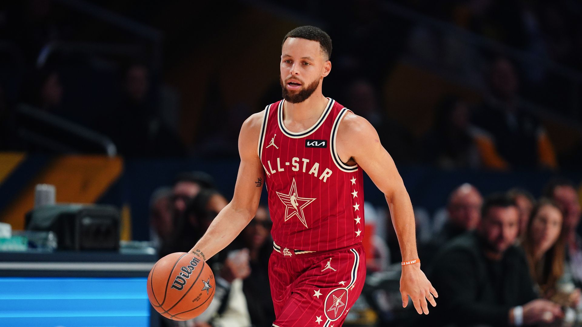 Steph Curry in a red All star uniform dribbles the ball