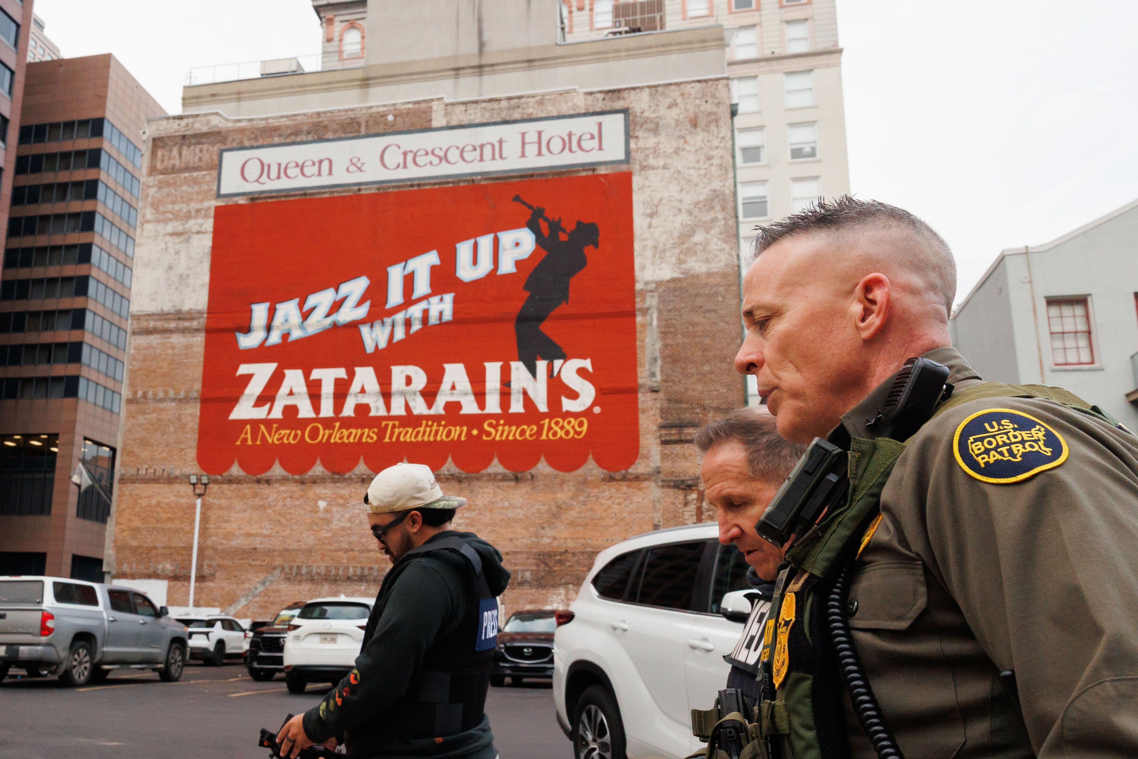 A uniformed man with a U.S. Border Patrol badge on his shoulder walks past a building with an advertisement Zatarain's painted on the side. 