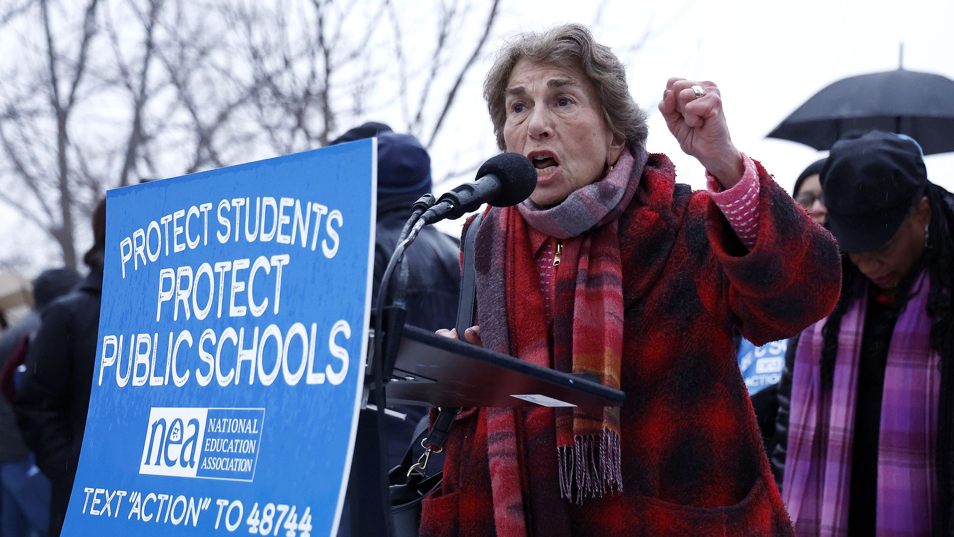 Photo of a woman behind a podium speaking outside into a microphone.