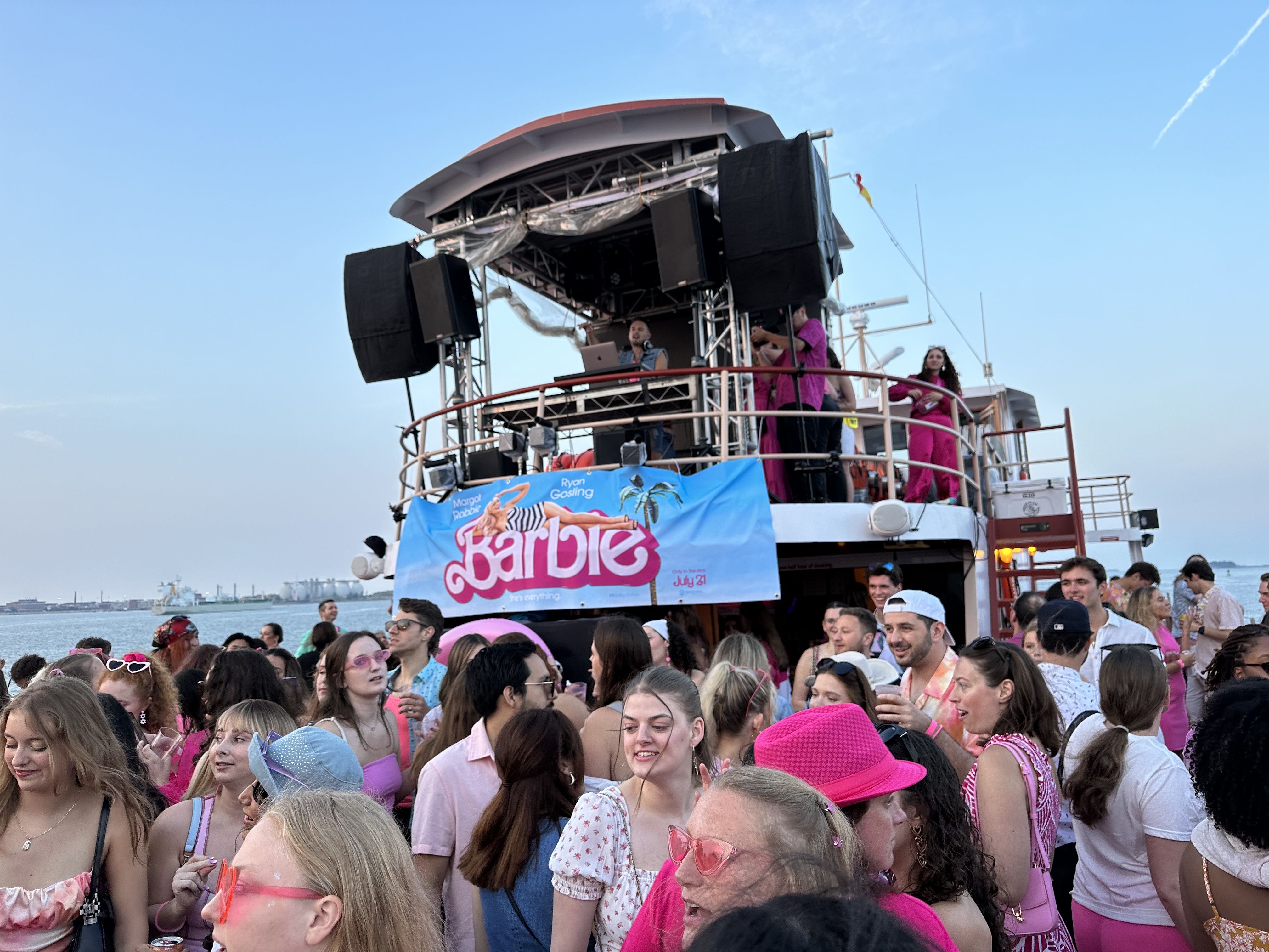 Hundreds dance and hang around the Barbie boat cruise Friday night. A DJ plays music, near a large Barbie banner.