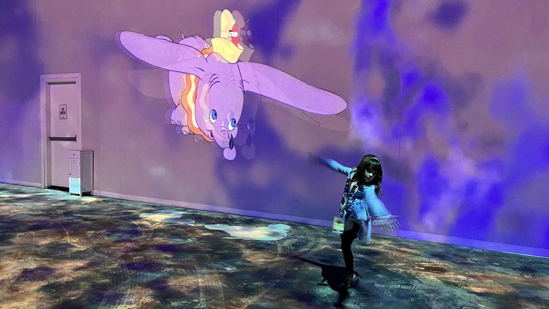 A child dances in front of a projection of Dumbo.