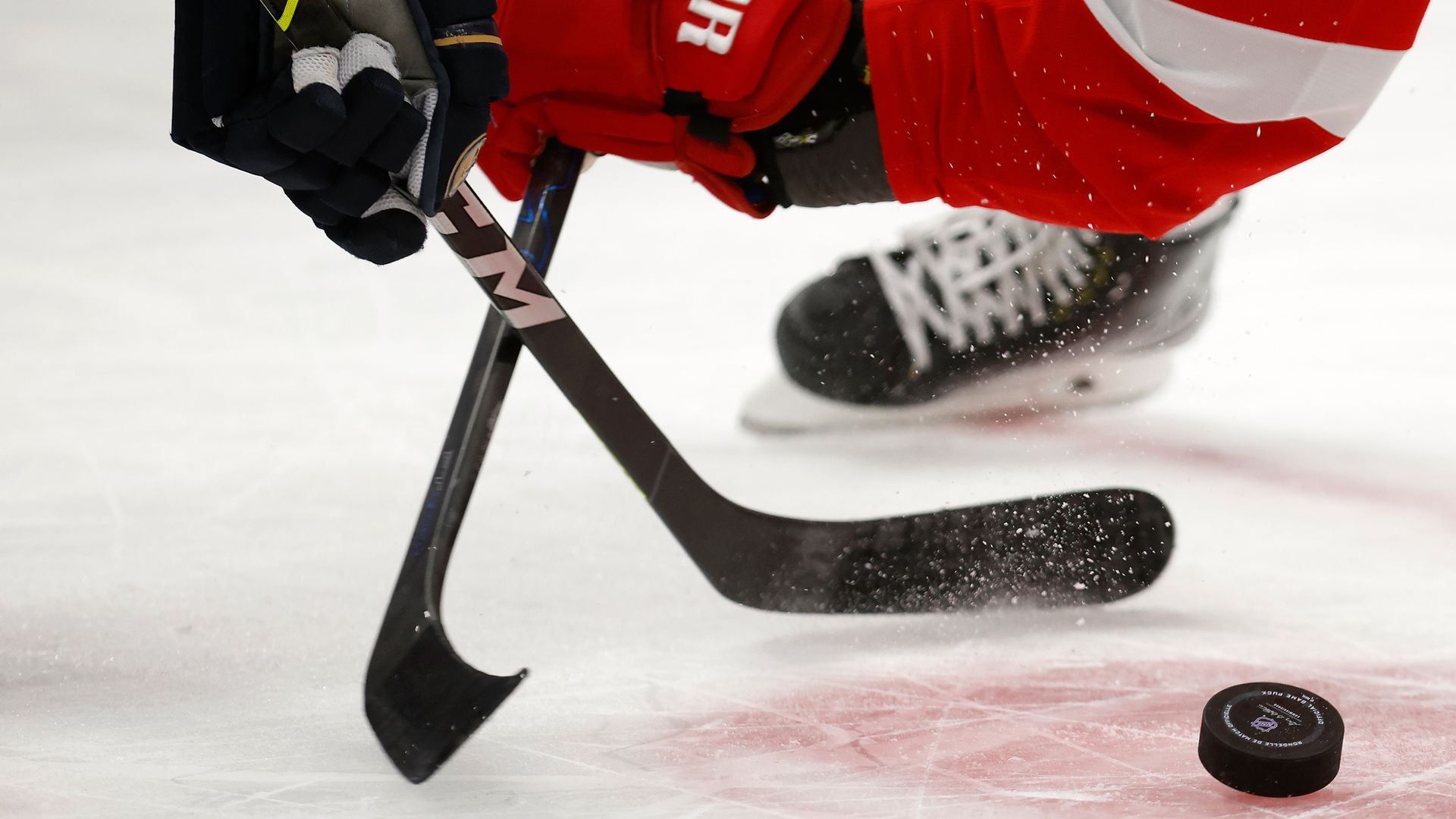 Two hockey sticks held by opposing players reach for a puck.