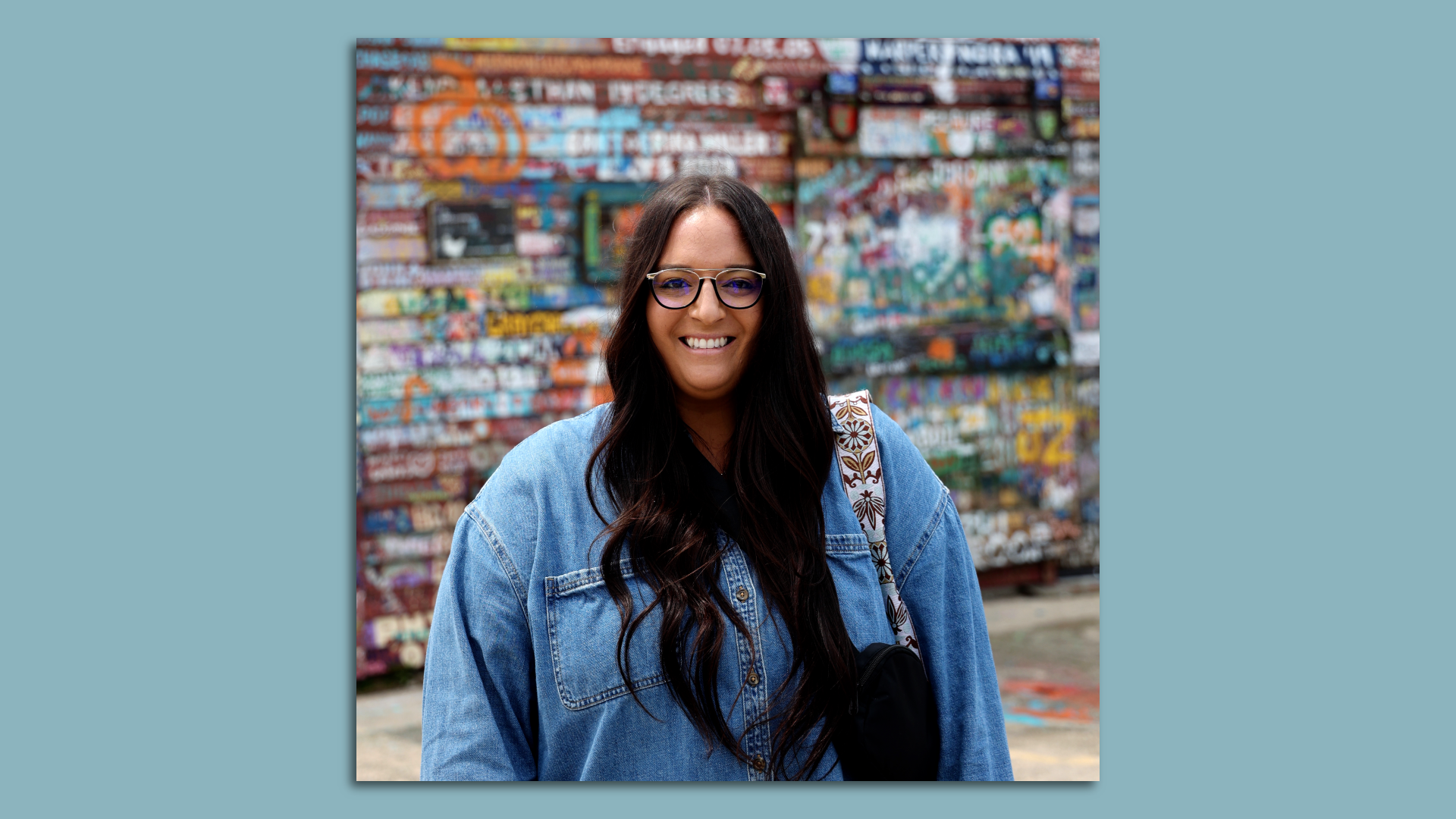 A photo of Lizanne, a woman with long brown hair and black glasses wearing a blue denim shirt.