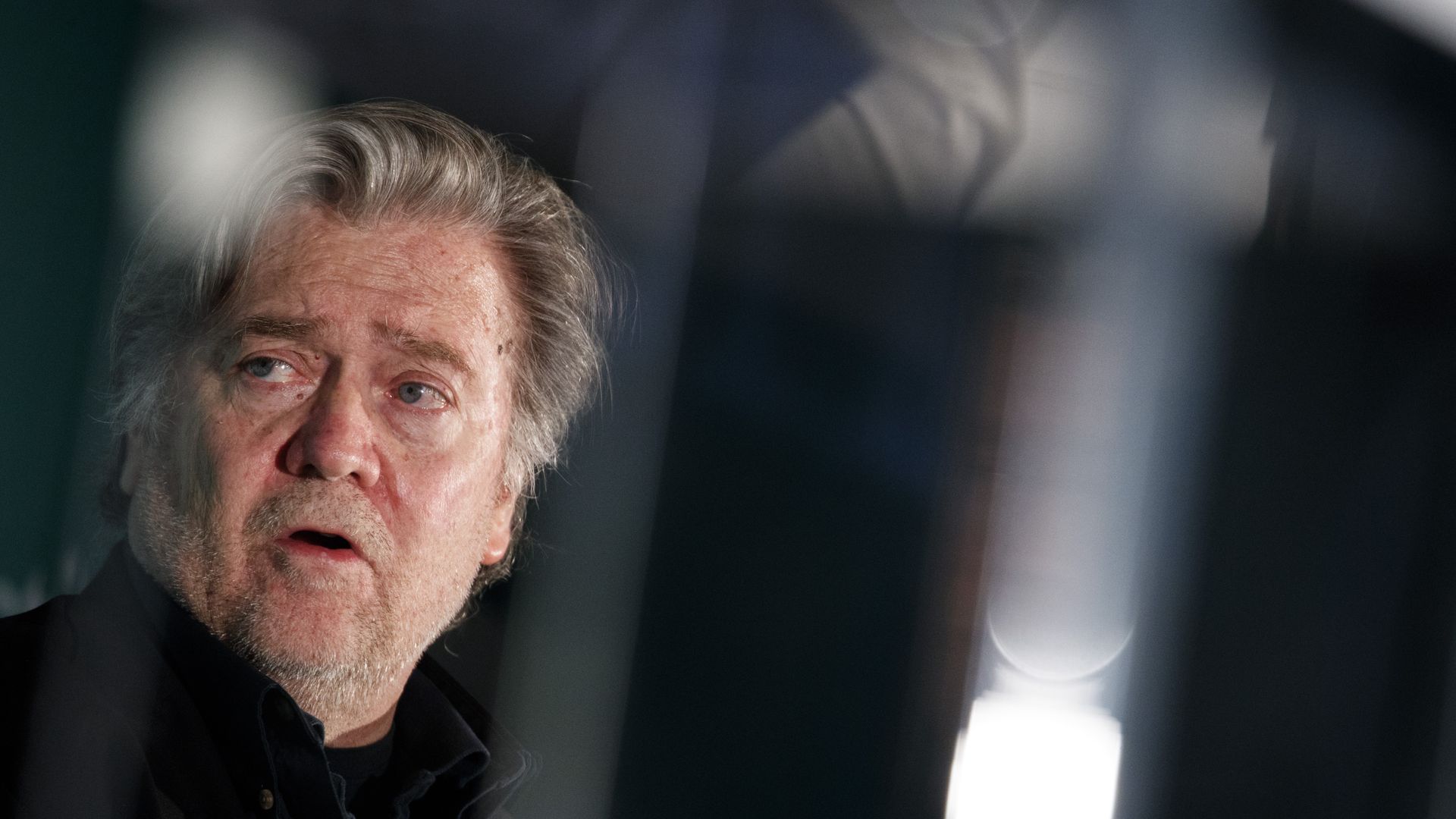 Steve Bannon in the far left side of the portrait looks over his right shoulder with his mouth open.