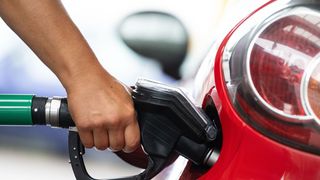 A person squeezes the handle of a gas pump while filling a red car. 