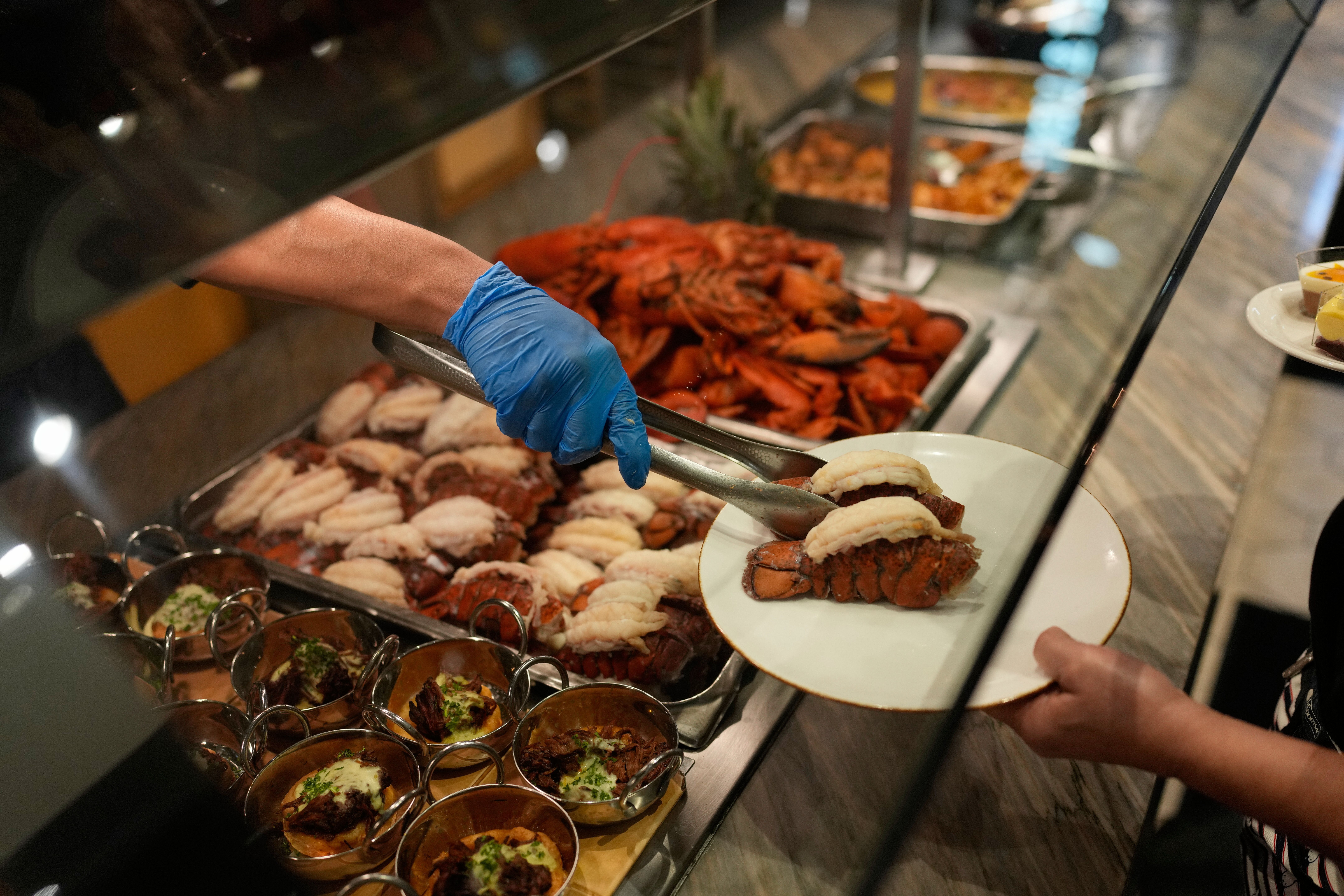 An aerial view of a server using tongs to place a lobster tail on an outstretched plate