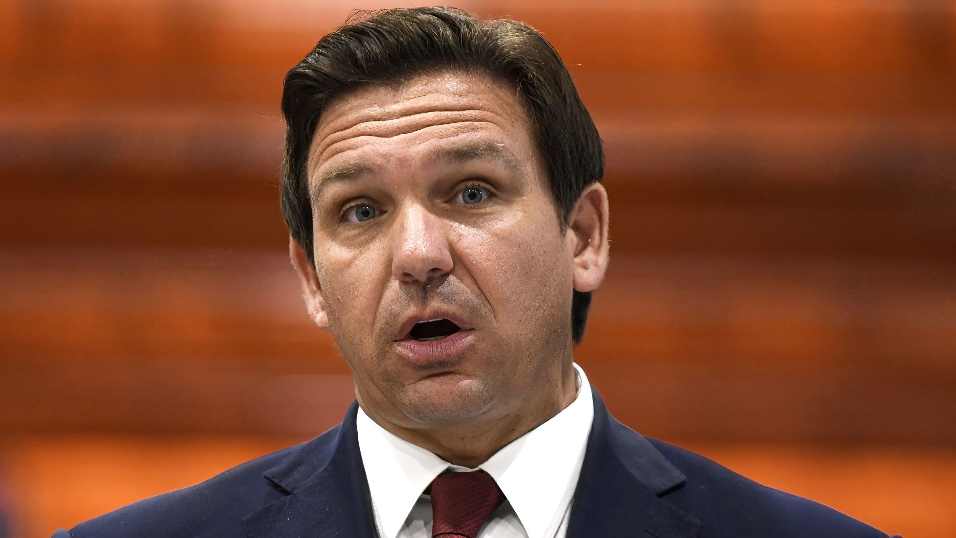 Ron DeSantis stands in a suit while talking