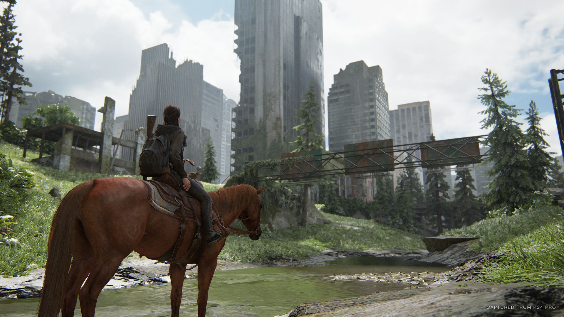 A screenshot of the video game "The Last of Us Part II," depicting player character Ellie riding a horse and overlooking an abandoned city.