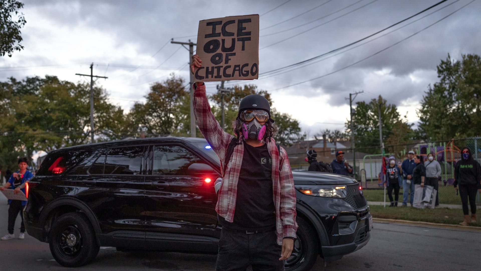 Photo of a protester in front of a police car with a sign that says "Ice Out of Chicago." 