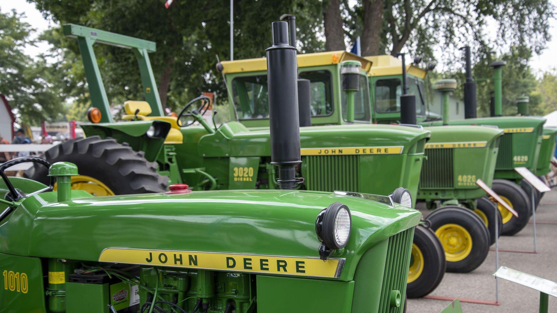 Green tractors sit in a row at a fair