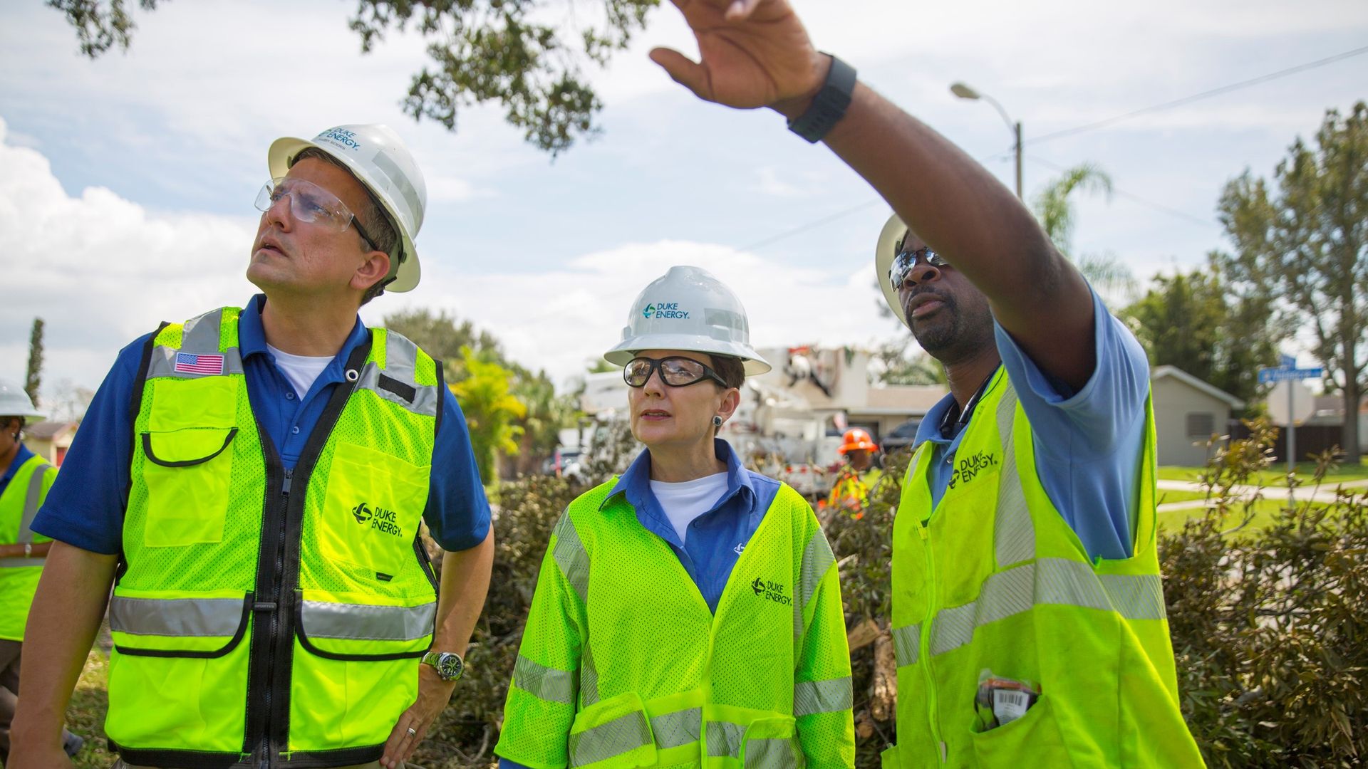 Lynn Good (center) stands with two men on a Duke Energy site. All three are in hard hats, bright yellow vests and blue shirts. 
