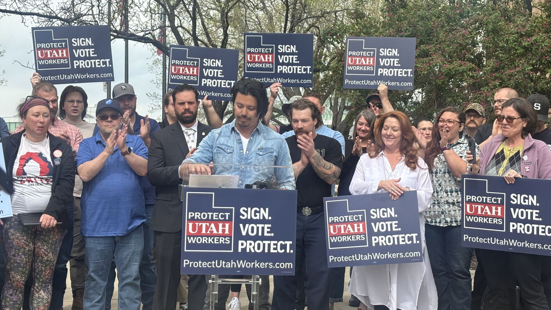 A group of people hold up political signs that say "sign vote protect"